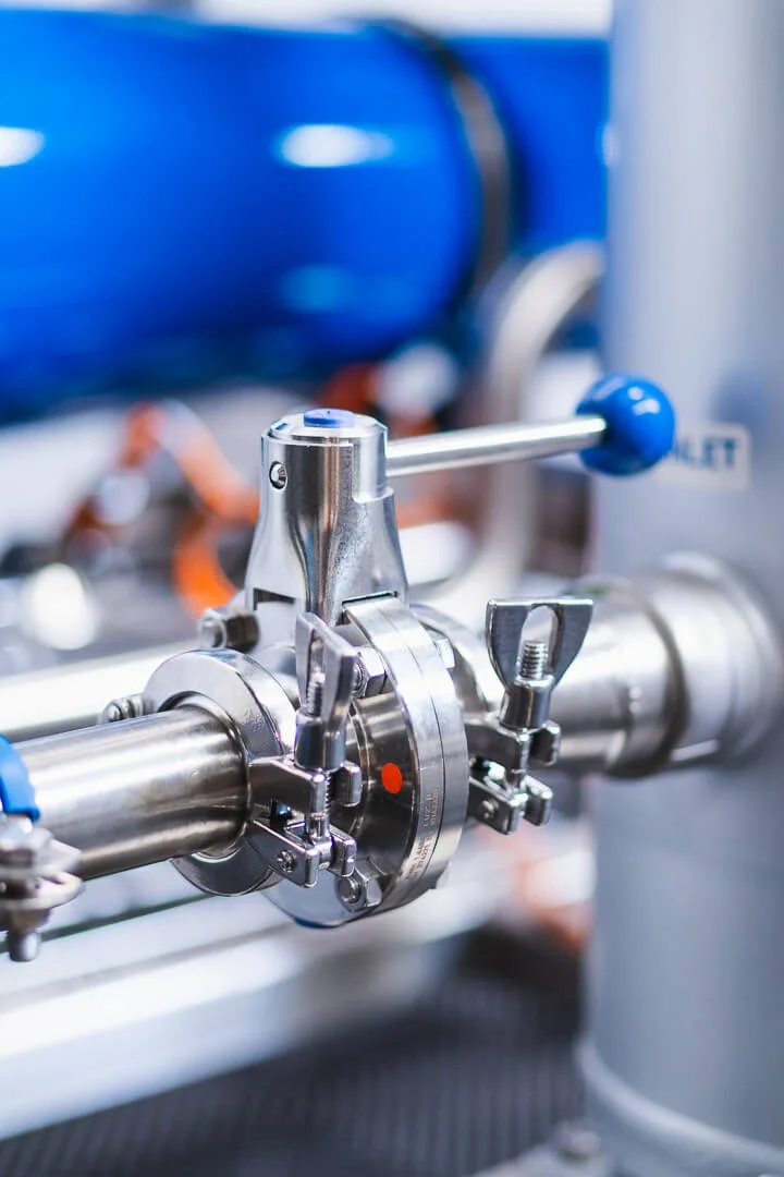 Close-up of a stainless steel industrial valve with blue handles, used in a pipeline system.