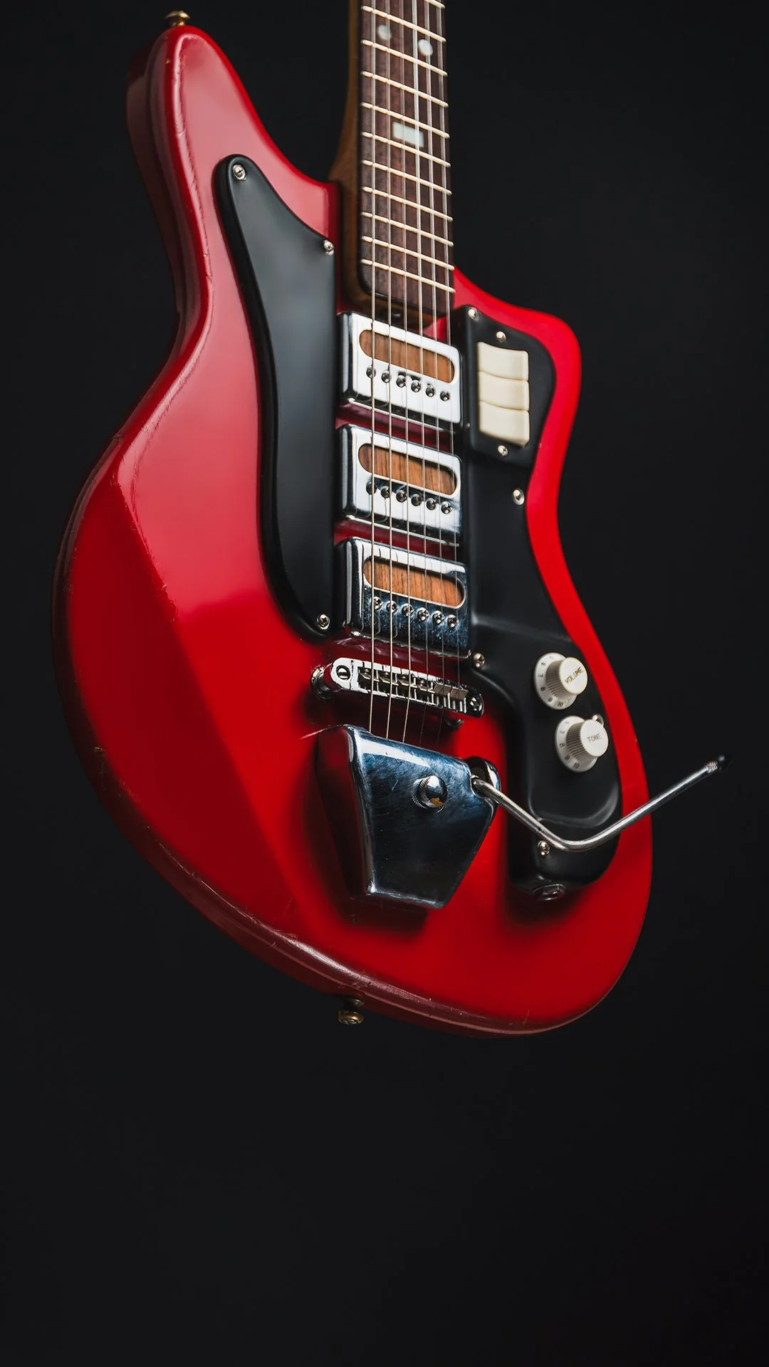 Red electric guitar with black, white, and chrome details against a black background.