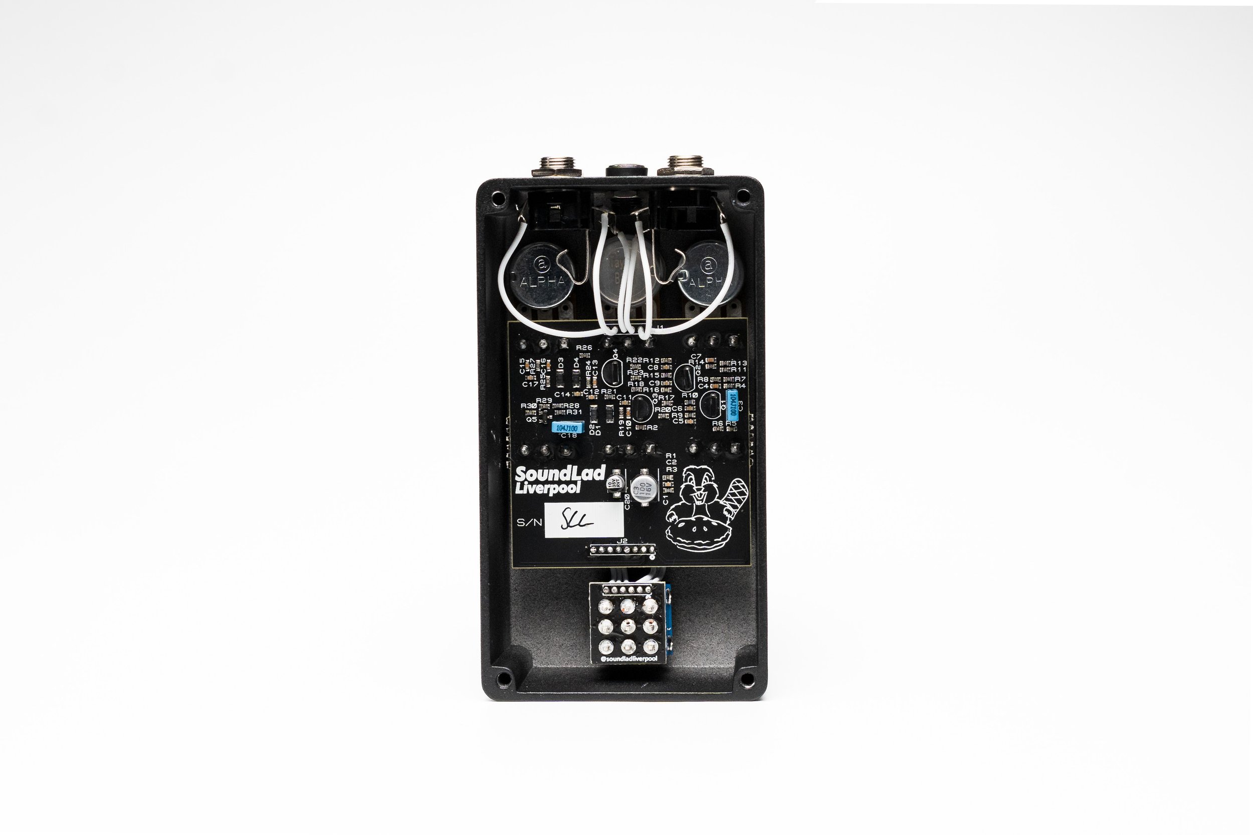 The interior of an electronic sound device with visible circuit board, wires, and circular components, branded SoundLad Liverpool, with a cartoon graphic of a happy face wearing headphones on the circuit board.