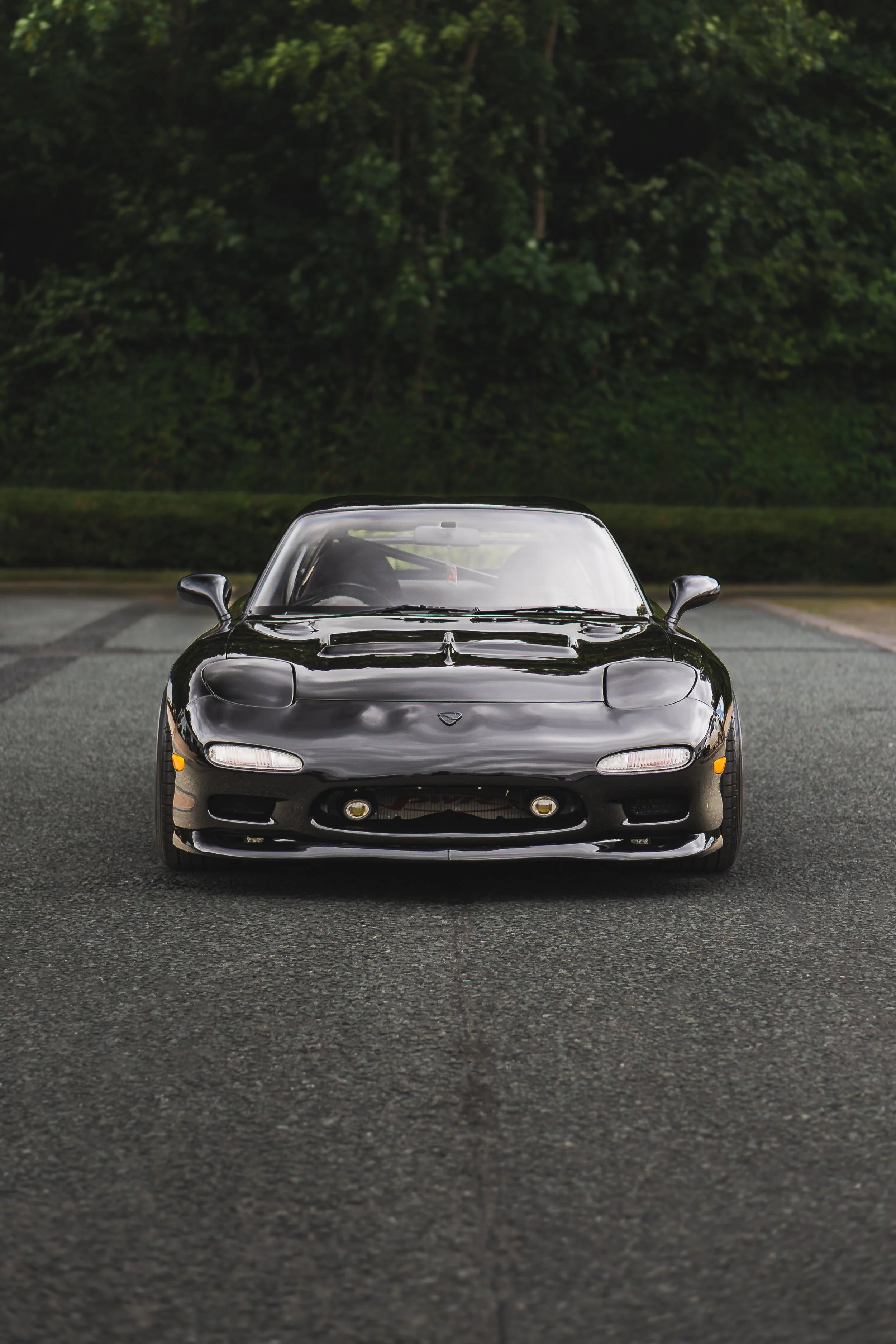 Black sports car parked on an asphalt road with a green wooded background.