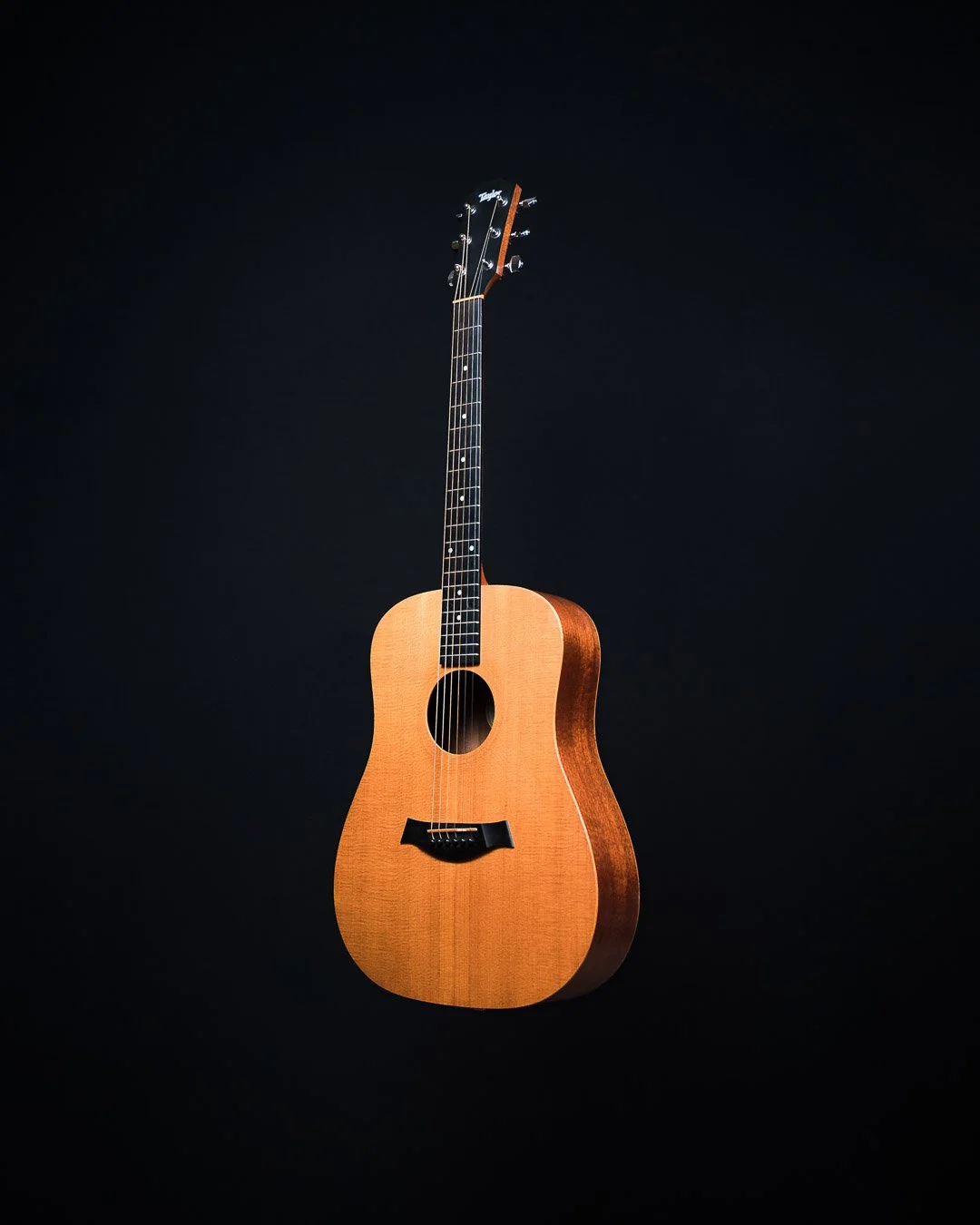 An acoustic guitar with a natural wood finish against a black background.