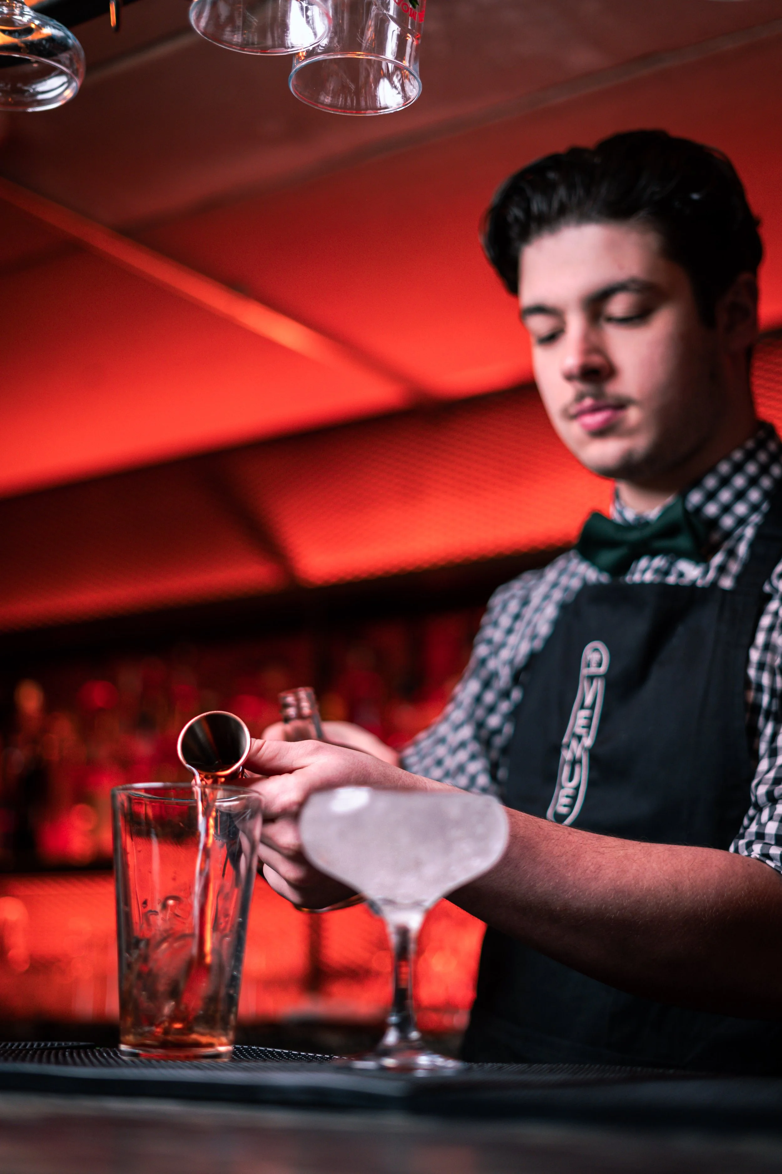 A bartender pouring a drink into a glass in a bar with red lighting.