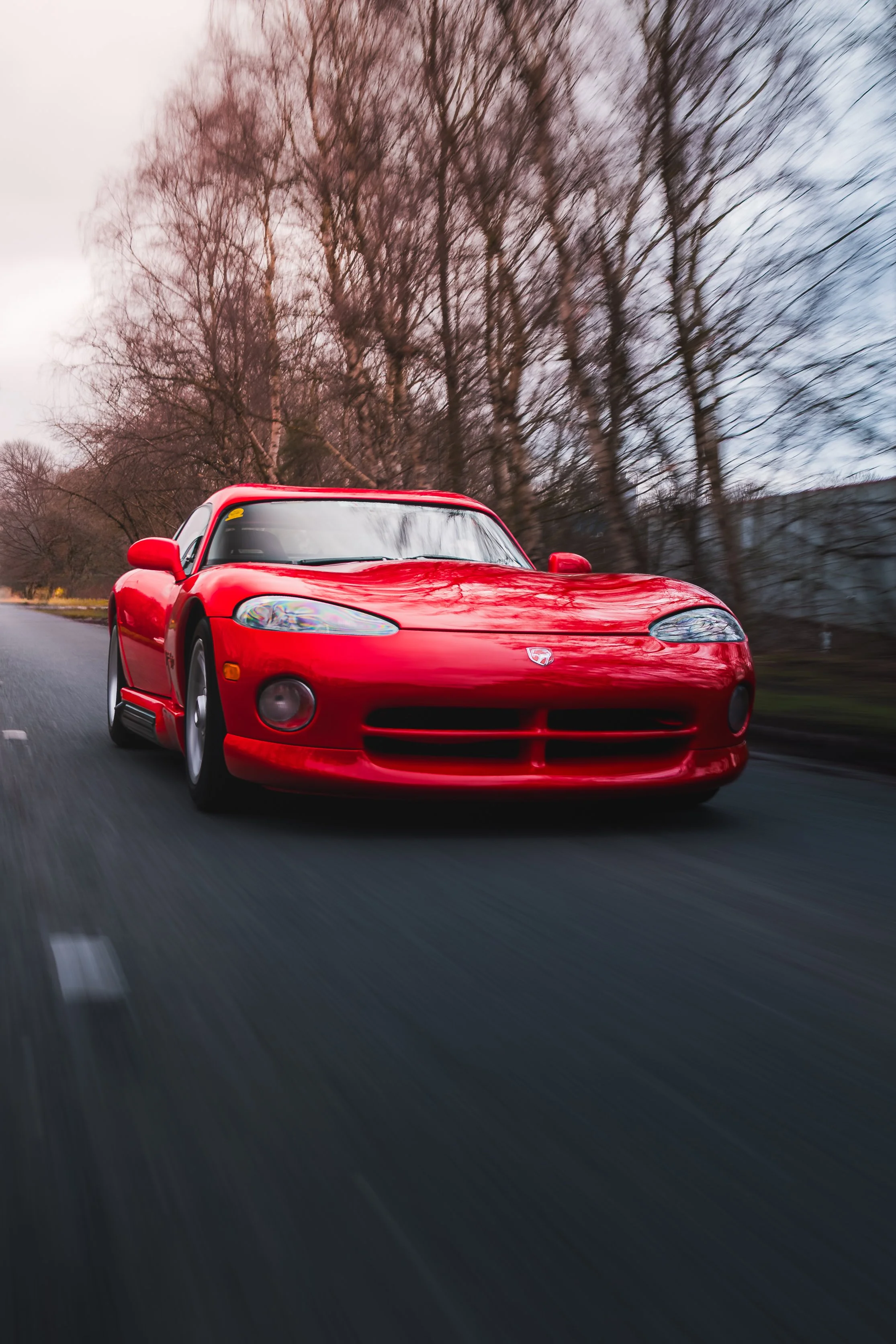 A red sports car driving on a road with trees in the background and a cloudy sky.