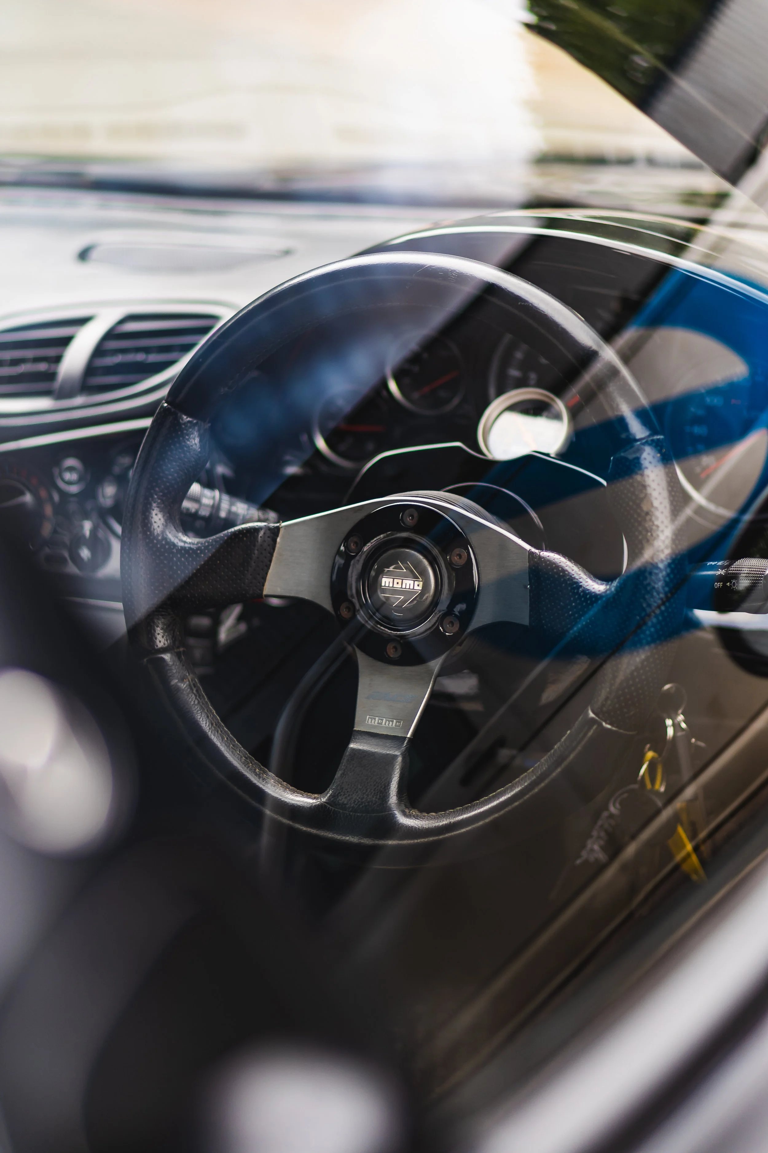 Close-up view of a car's steering wheel and dashboard, with a focus on the Momo brand steering wheel and instrument panel.
