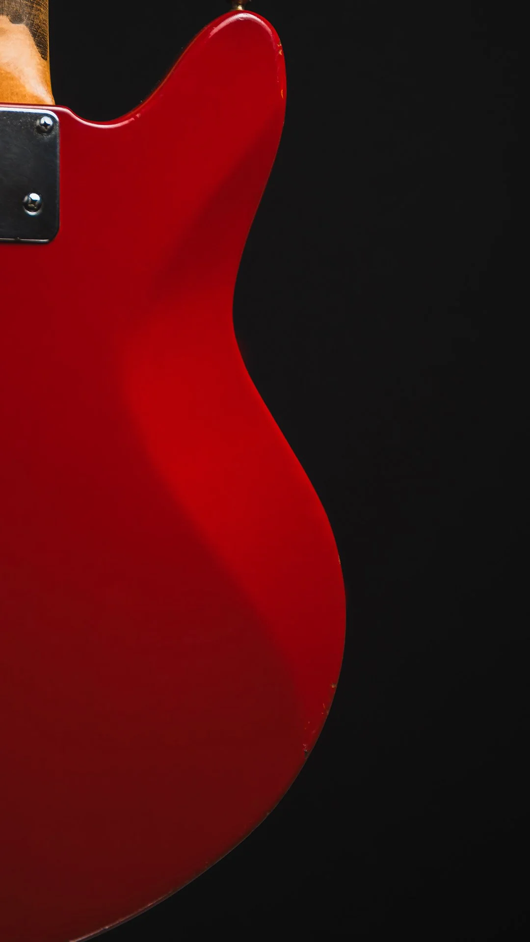 Close-up of the body of a red electric guitar with a black background.