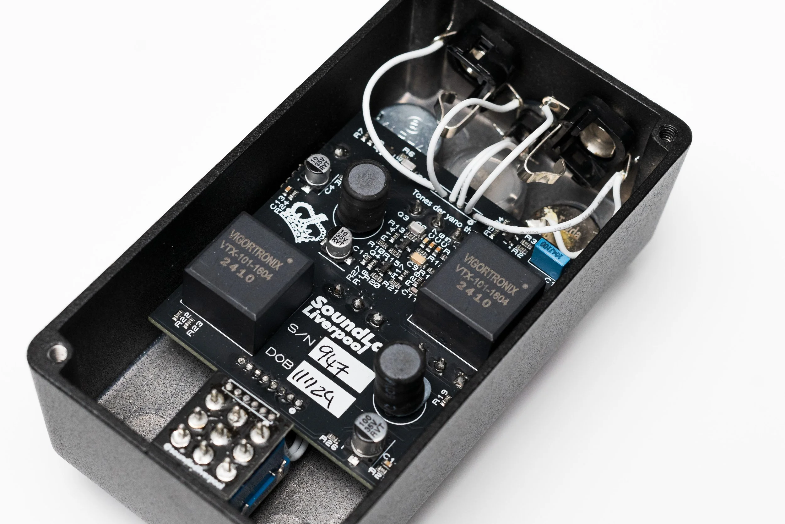Inside of an electronic guitar effects pedal with circuit board, relays, and wiring.