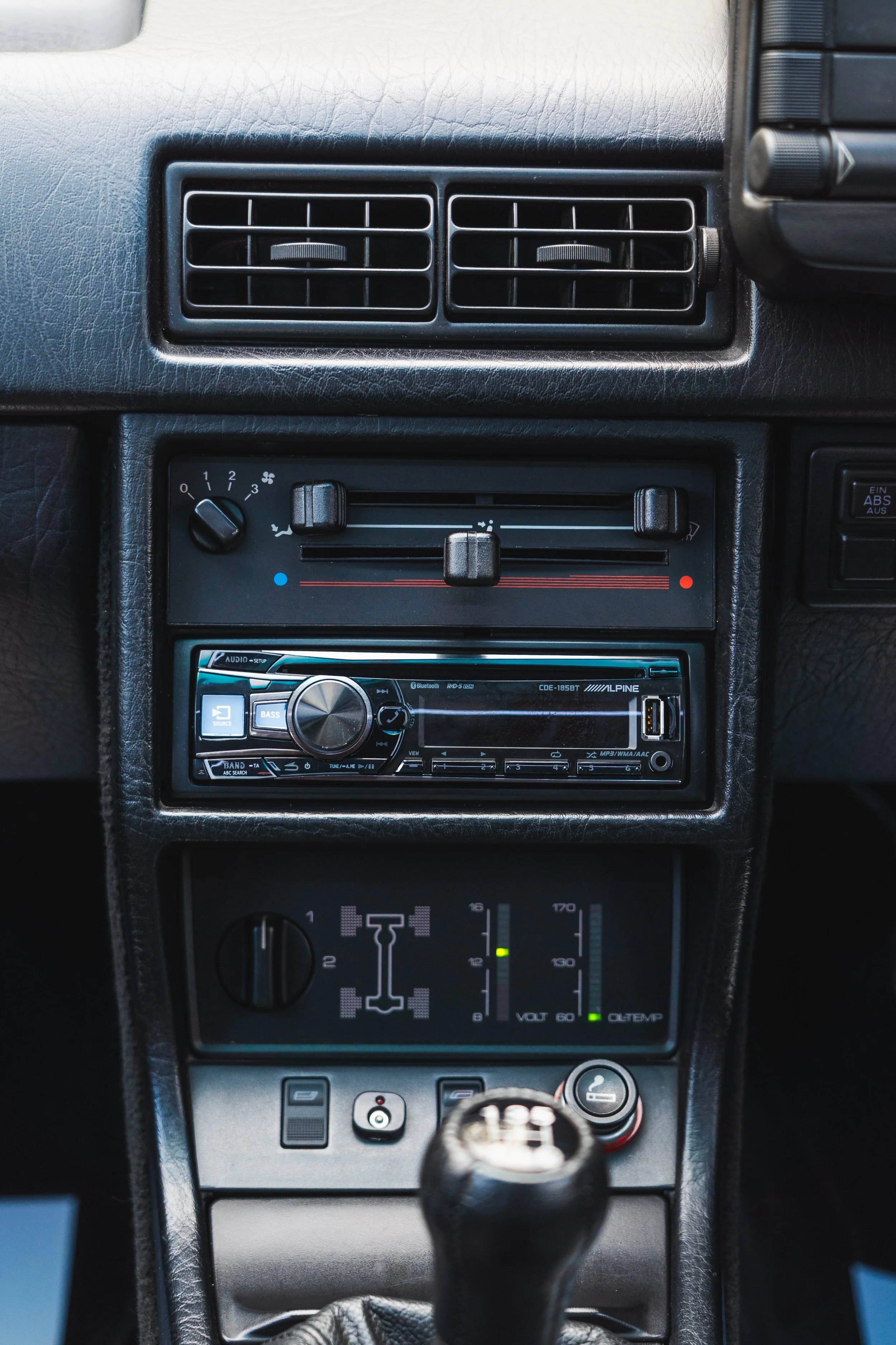 Close-up of car dashboard featuring air vents, climate controls, an Alpine stereo system, and various switches and gauges.