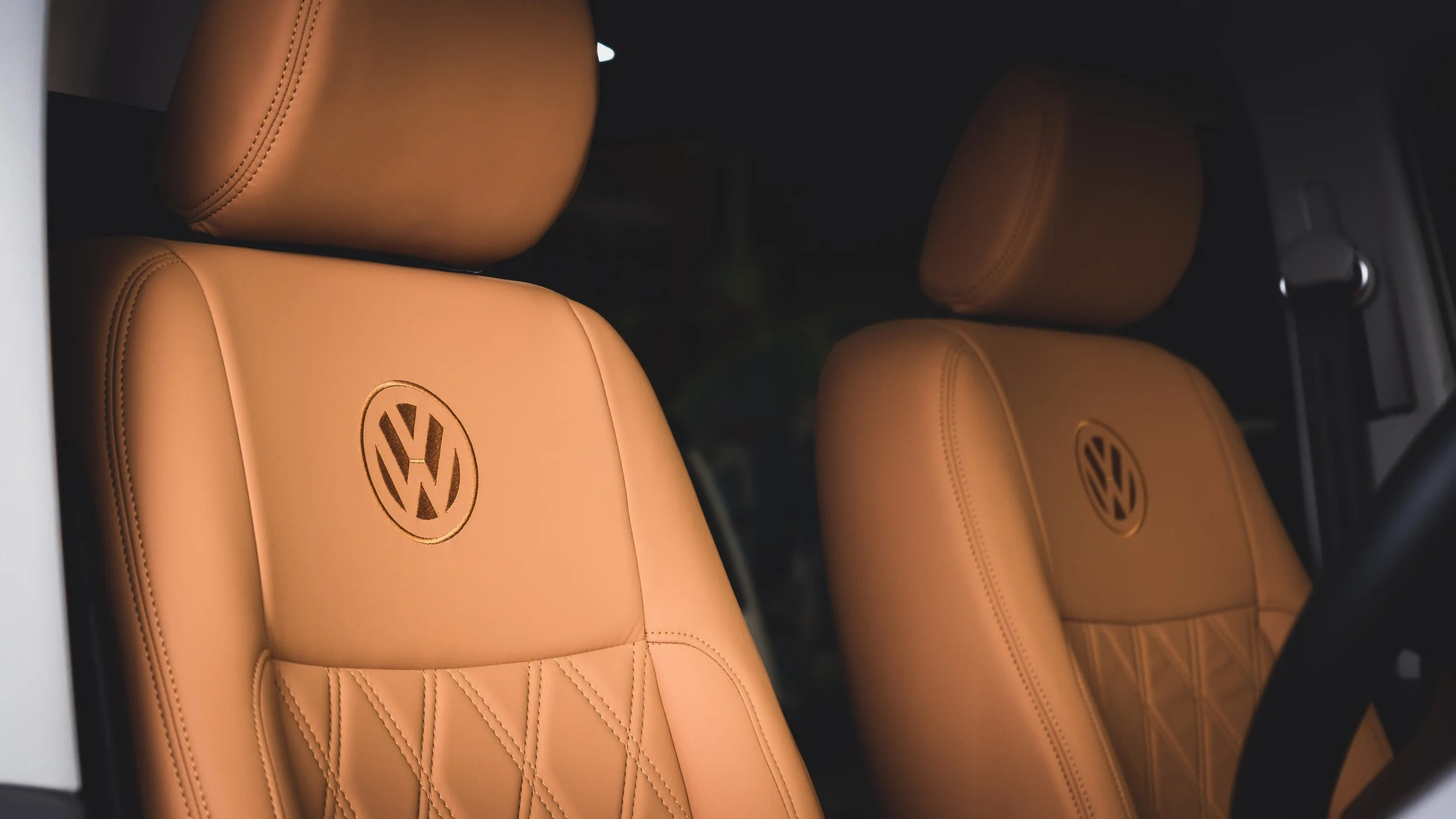 Close-up of tan leather Volkswagen car seats with a stitched diamond pattern and the VW logo embroidered on the headrests.