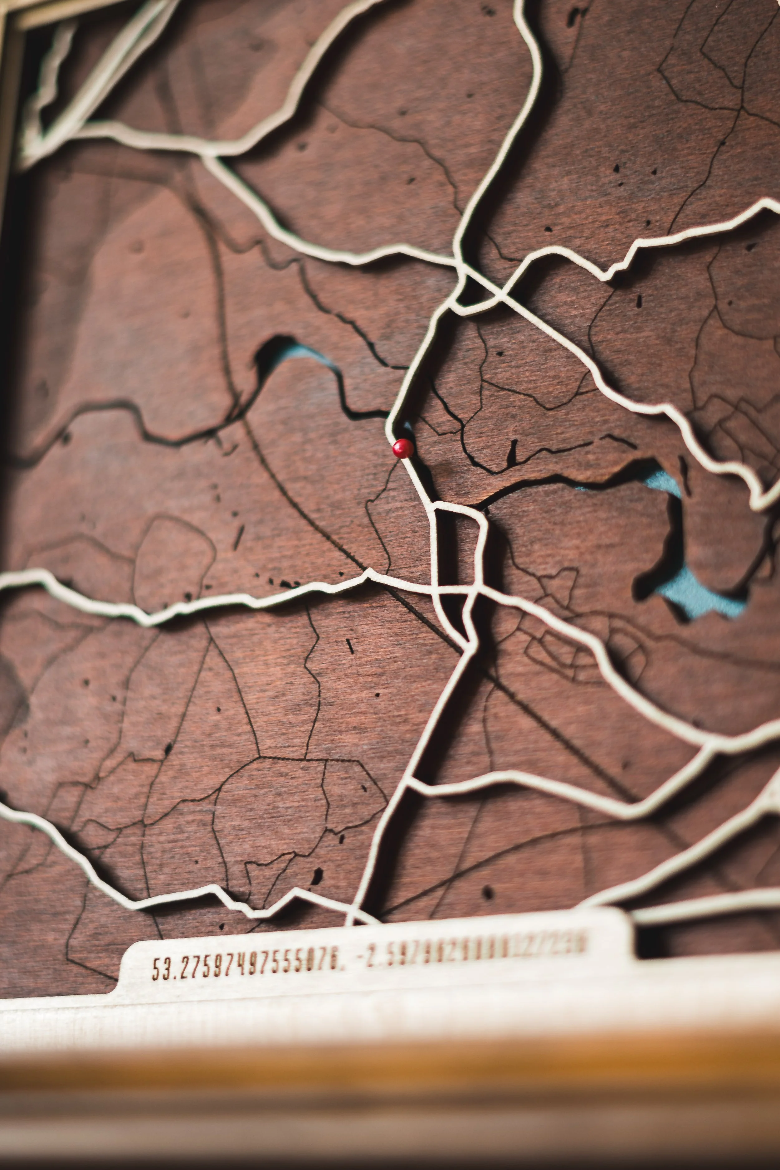 Close-up of a wooden map with metal outlines and listed coordinates at the bottom.