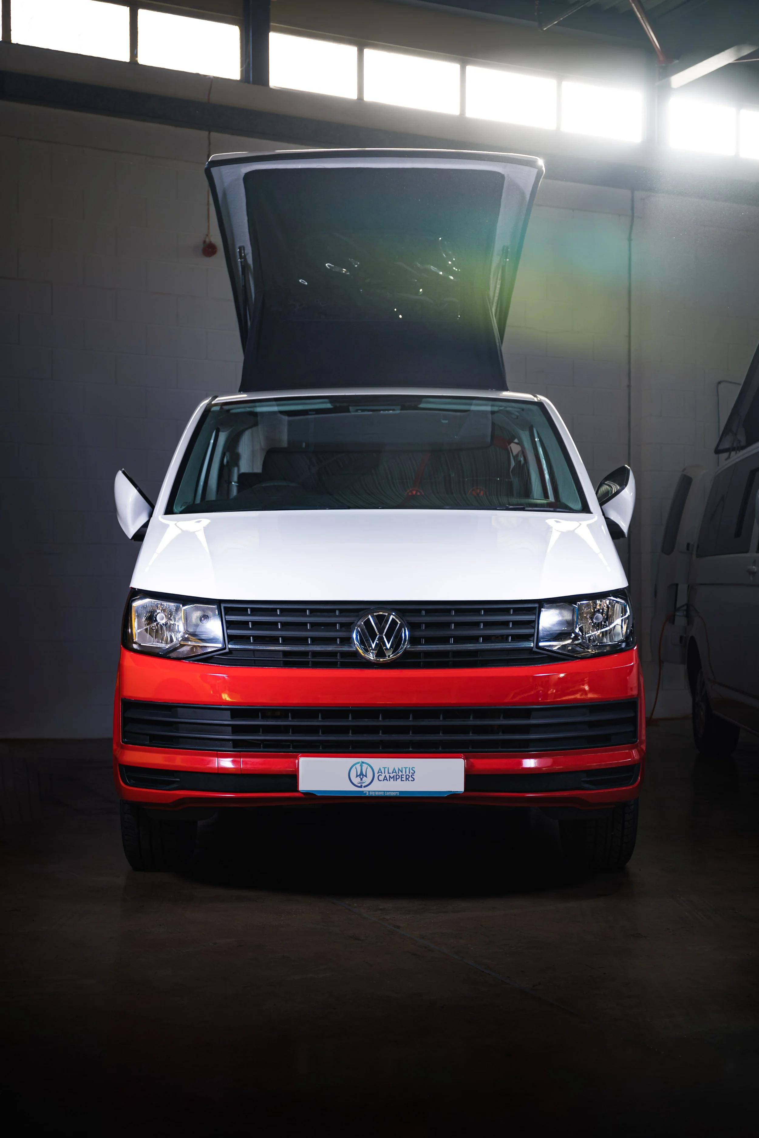 Front view of a Volkswagen camper van with an open roof hatch in a garage.
