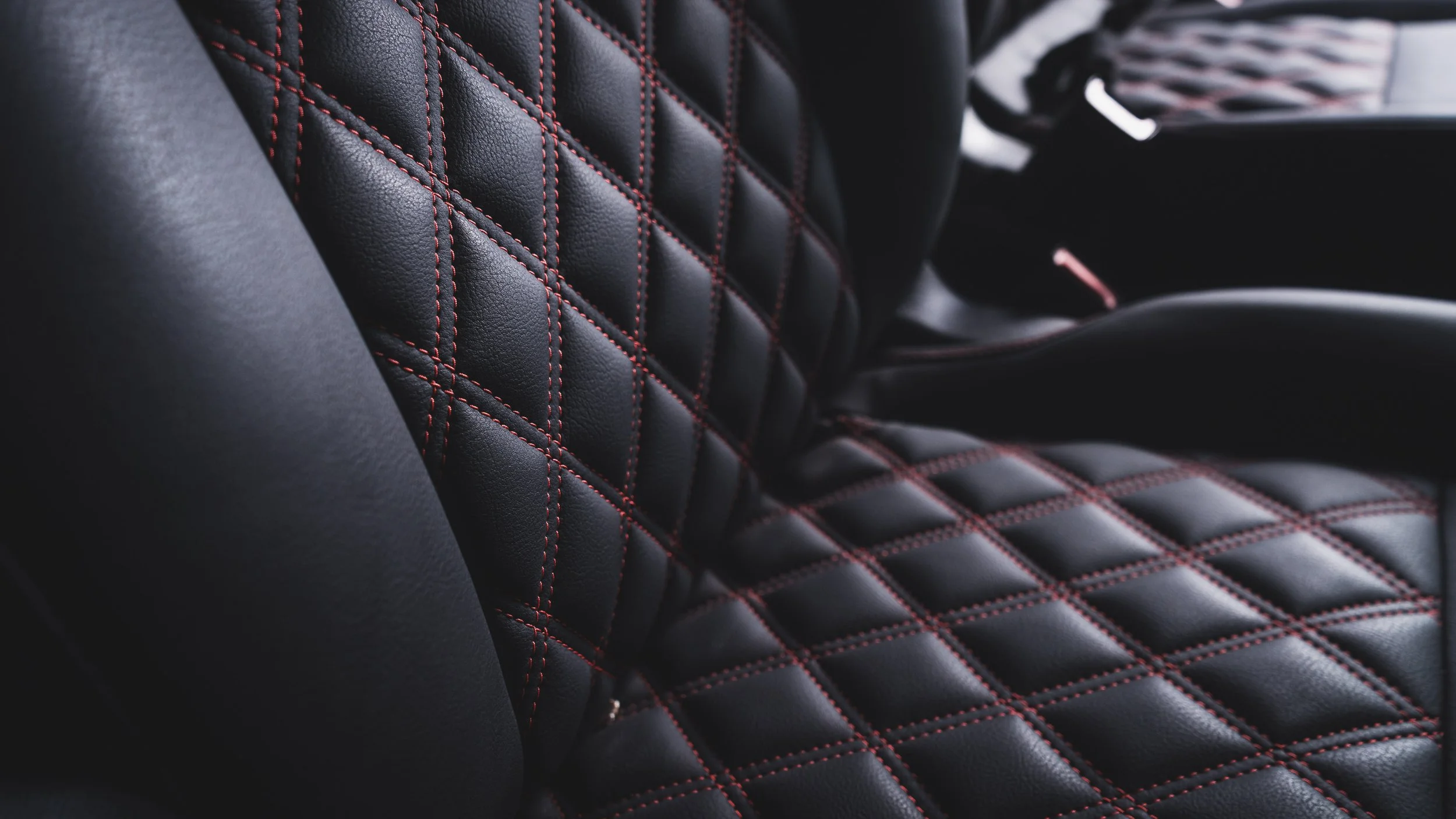 Close-up of a black car seat with diamond-patterned stitching in red.
