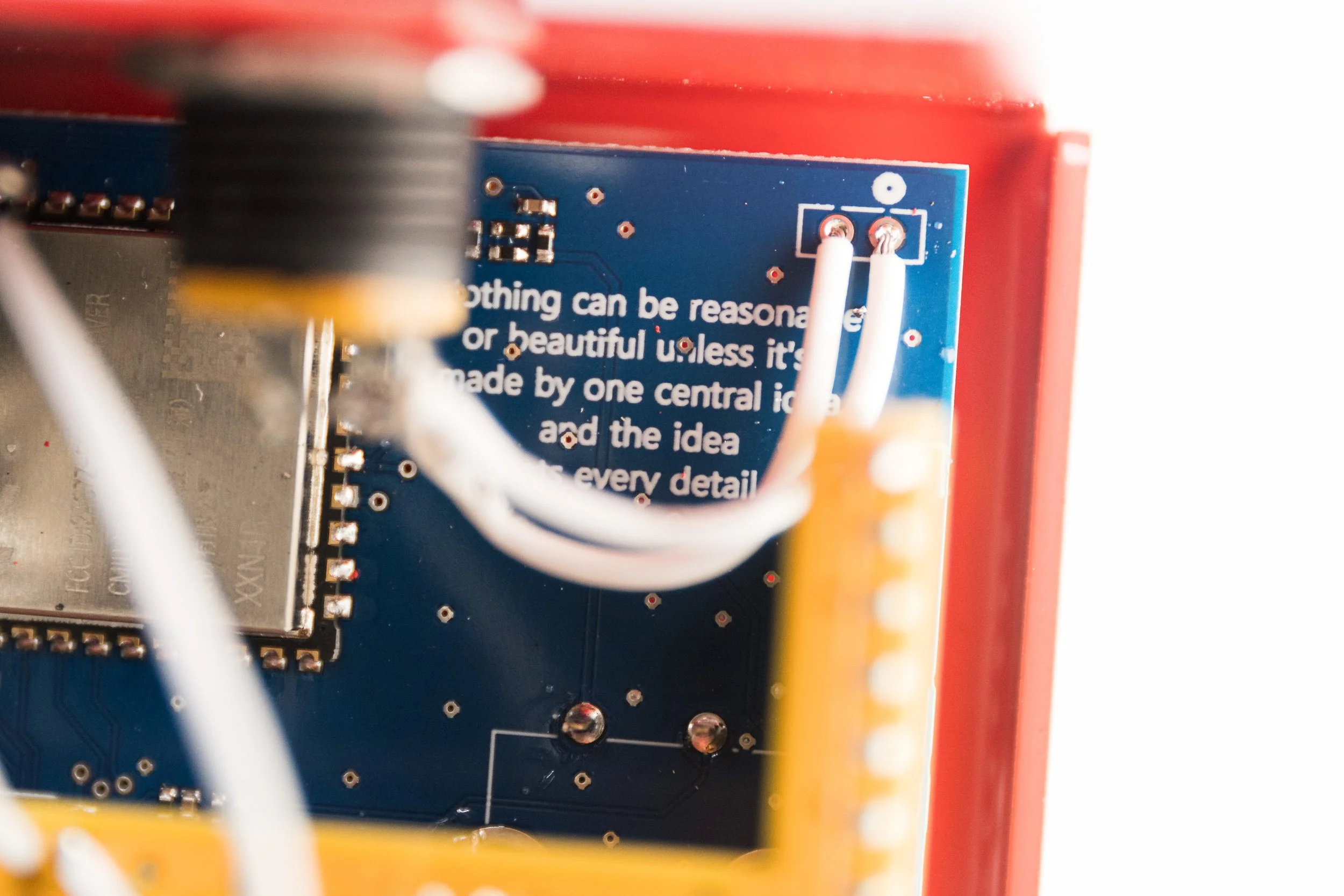 Close-up of an electronic circuit board with white wires connected, partially showing printed text with a motivational quote.