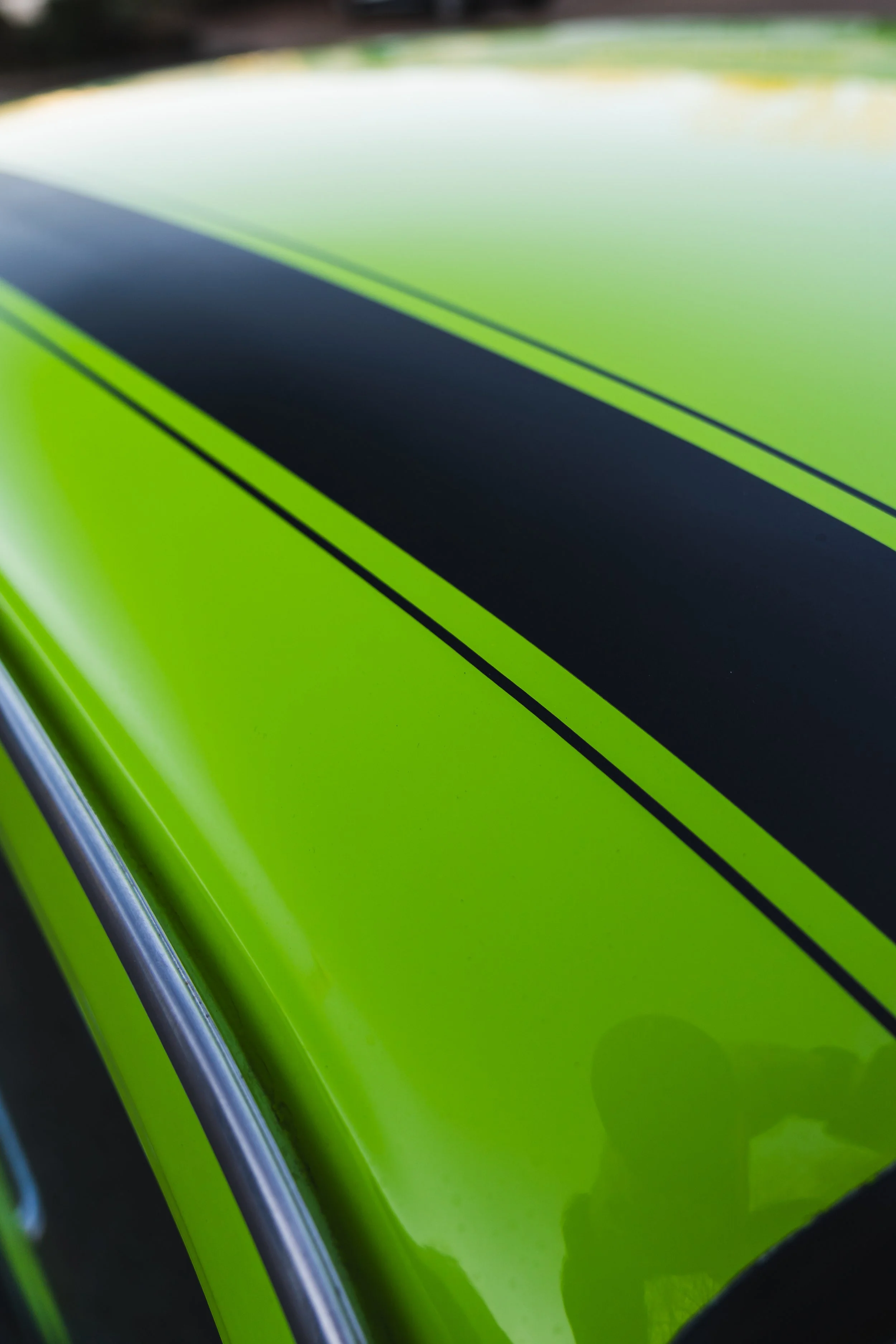 Close-up of a green and black racing stripe on a car's hood with a shiny, reflective surface.