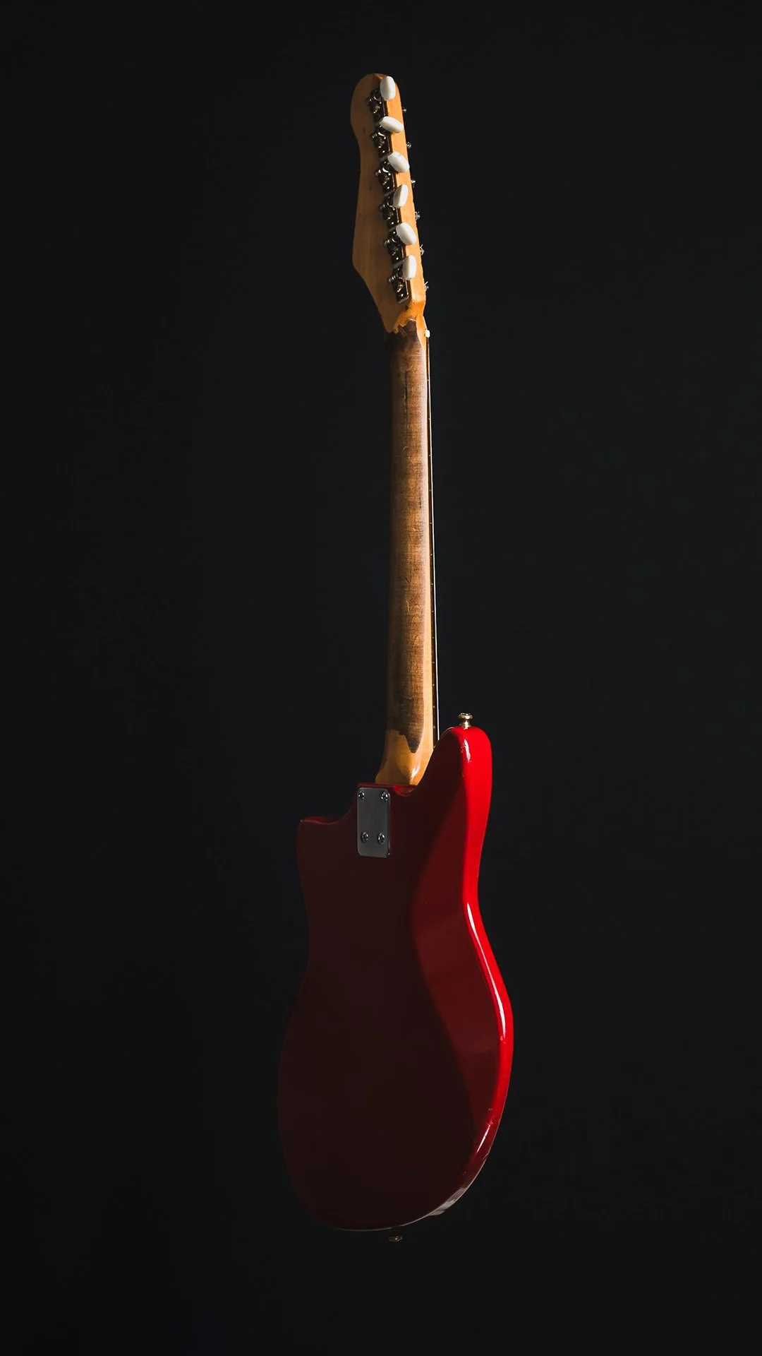 A red electric guitar viewed from the side against a black background.