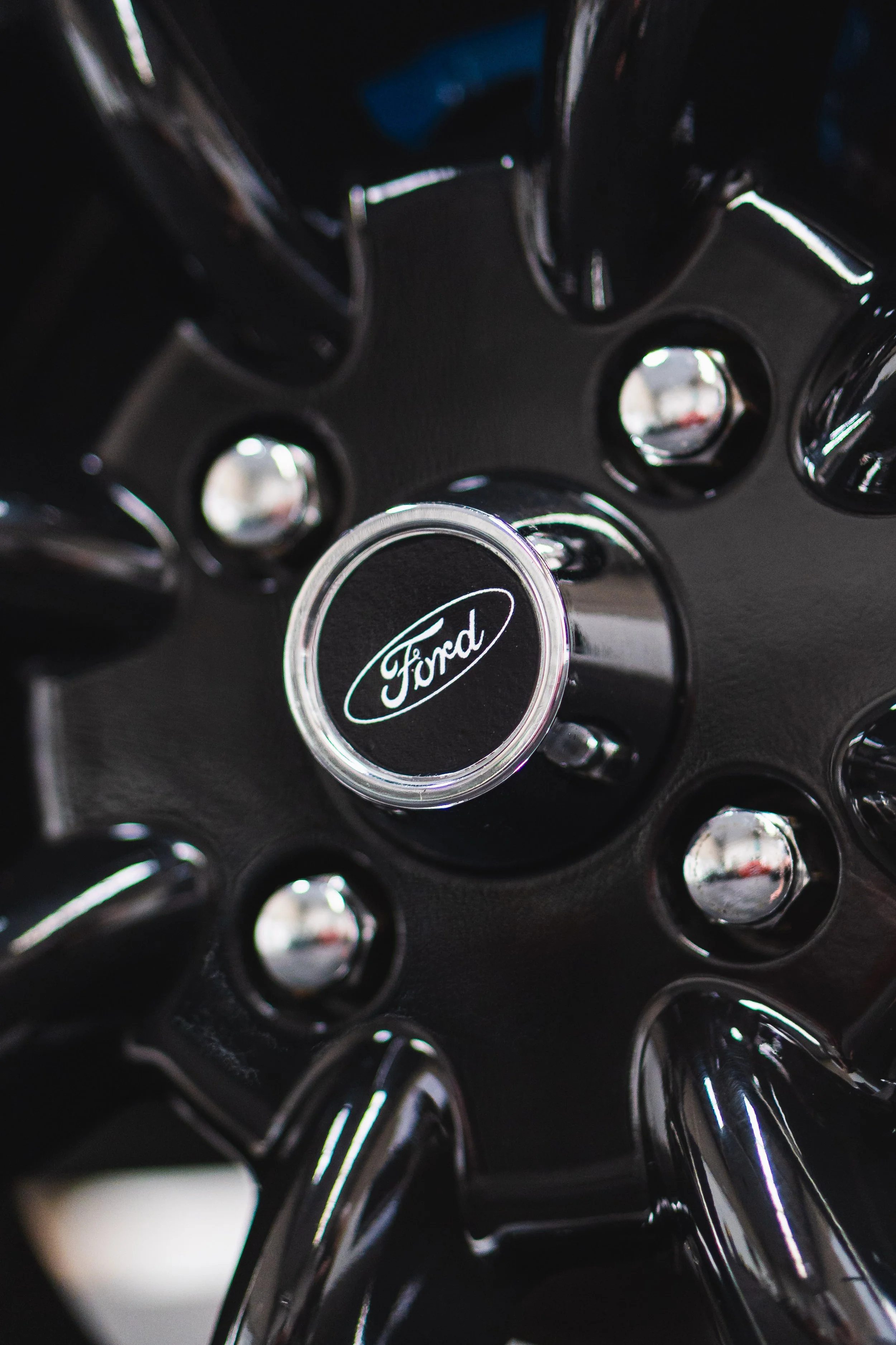 Close-up of a black Ford car wheel with chrome accents and the Ford logo in the center.