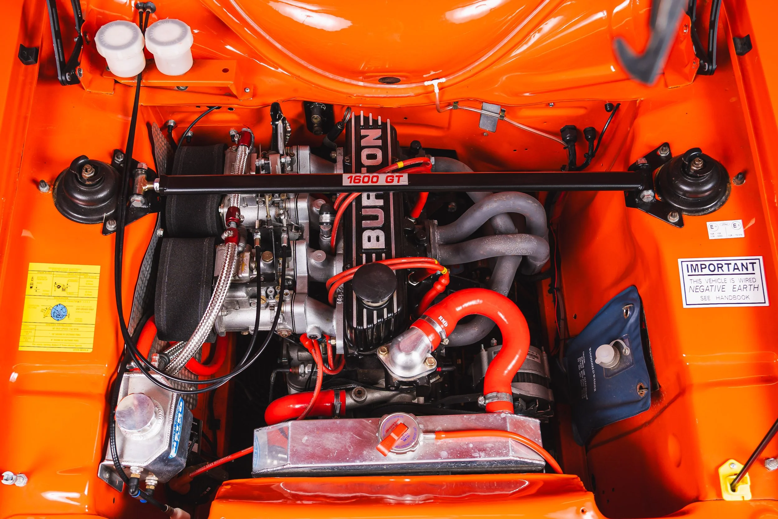 Close-up of a race car engine inside an orange engine bay, showing various components including hoses, wires, and labels.