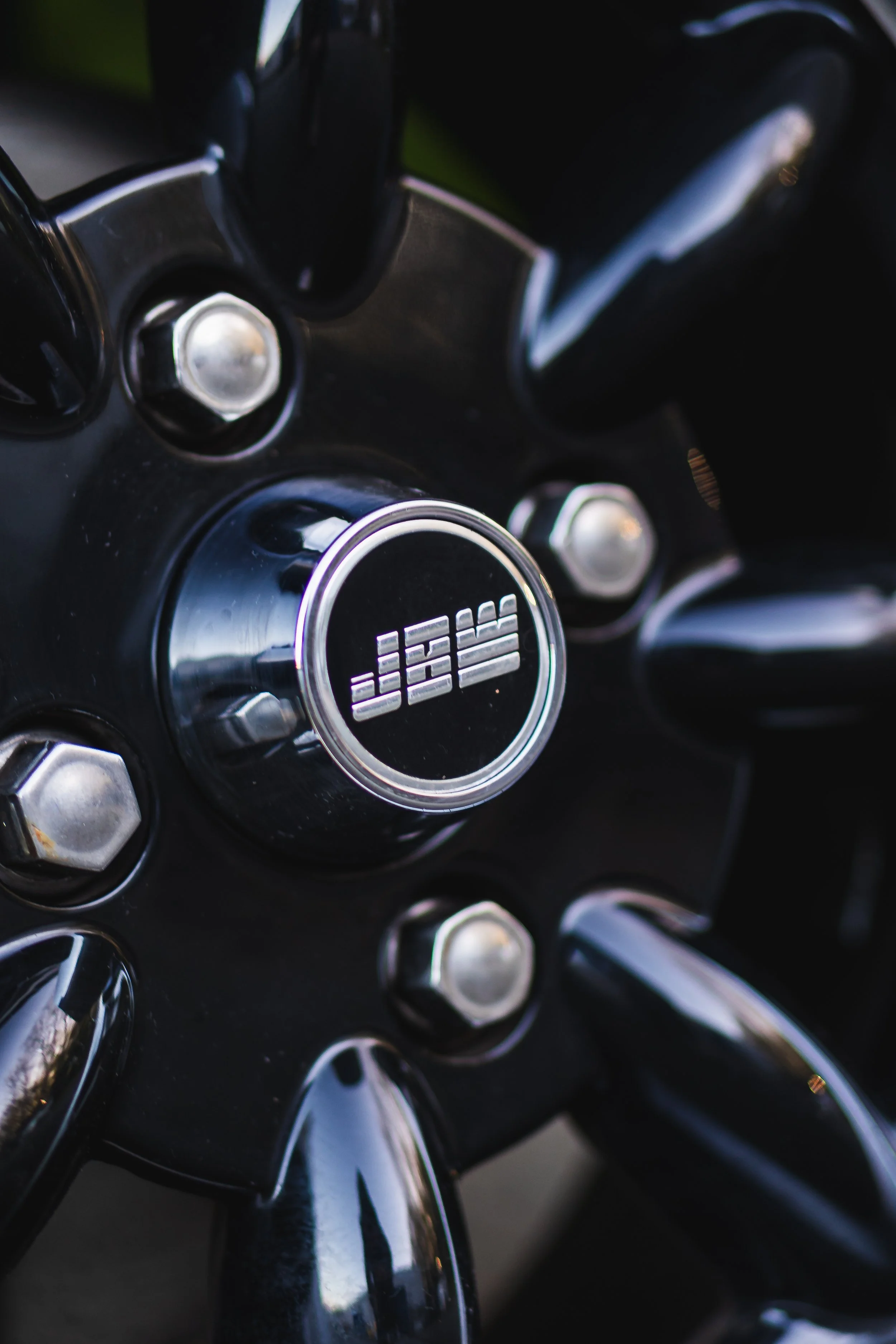 Close-up view of a black motorcycle wheel hub with chrome bolts and the brand name 'JBS' on the center cap.
