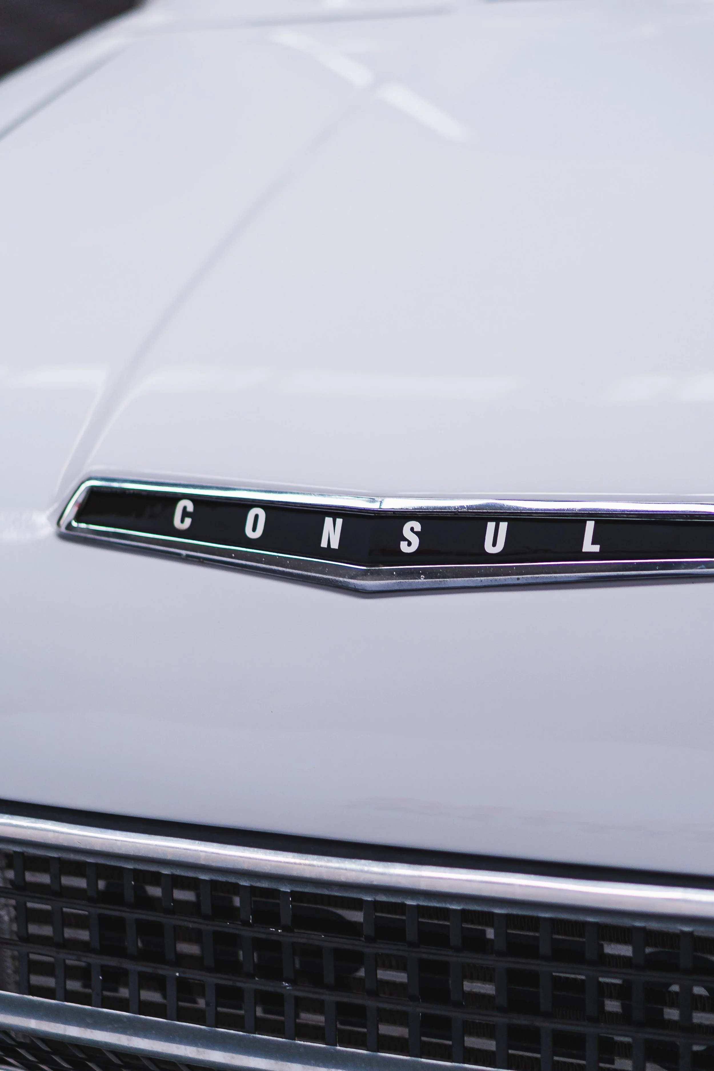 Close-up of a white car with a badge that spells out 'CONSUL' on the front grille.