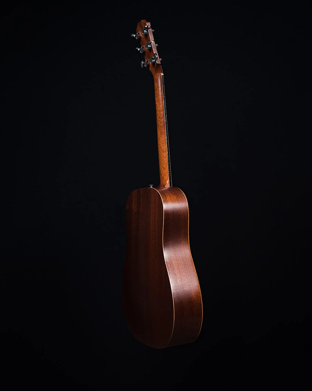 A wooden acoustic guitar hanging on a black background.