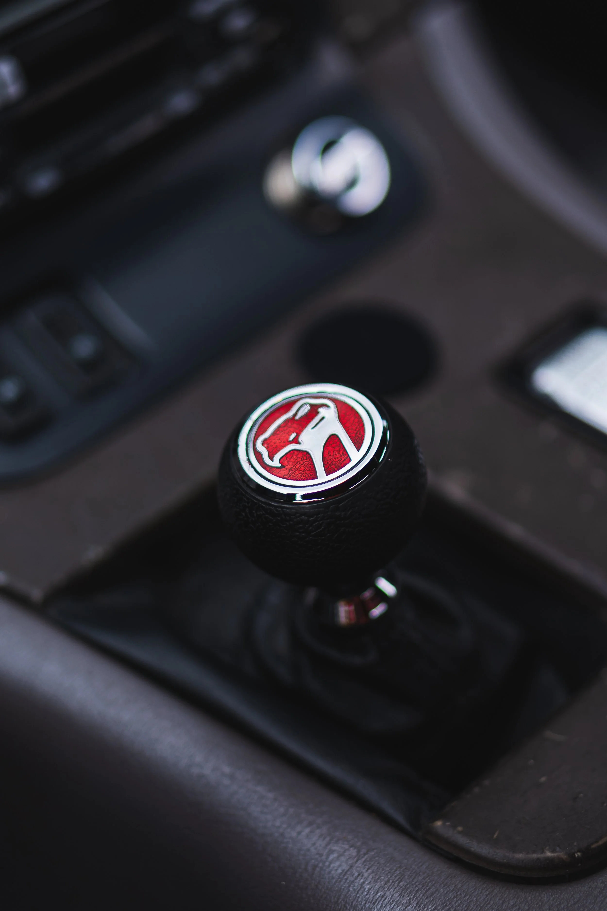 Close-up of a black car gear shift knob with a red and silver Pontiac emblem on top.
