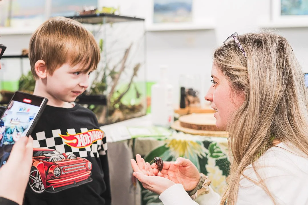 A woman showing a small chocolate treat to a young boy at an indoor event or exhibit.