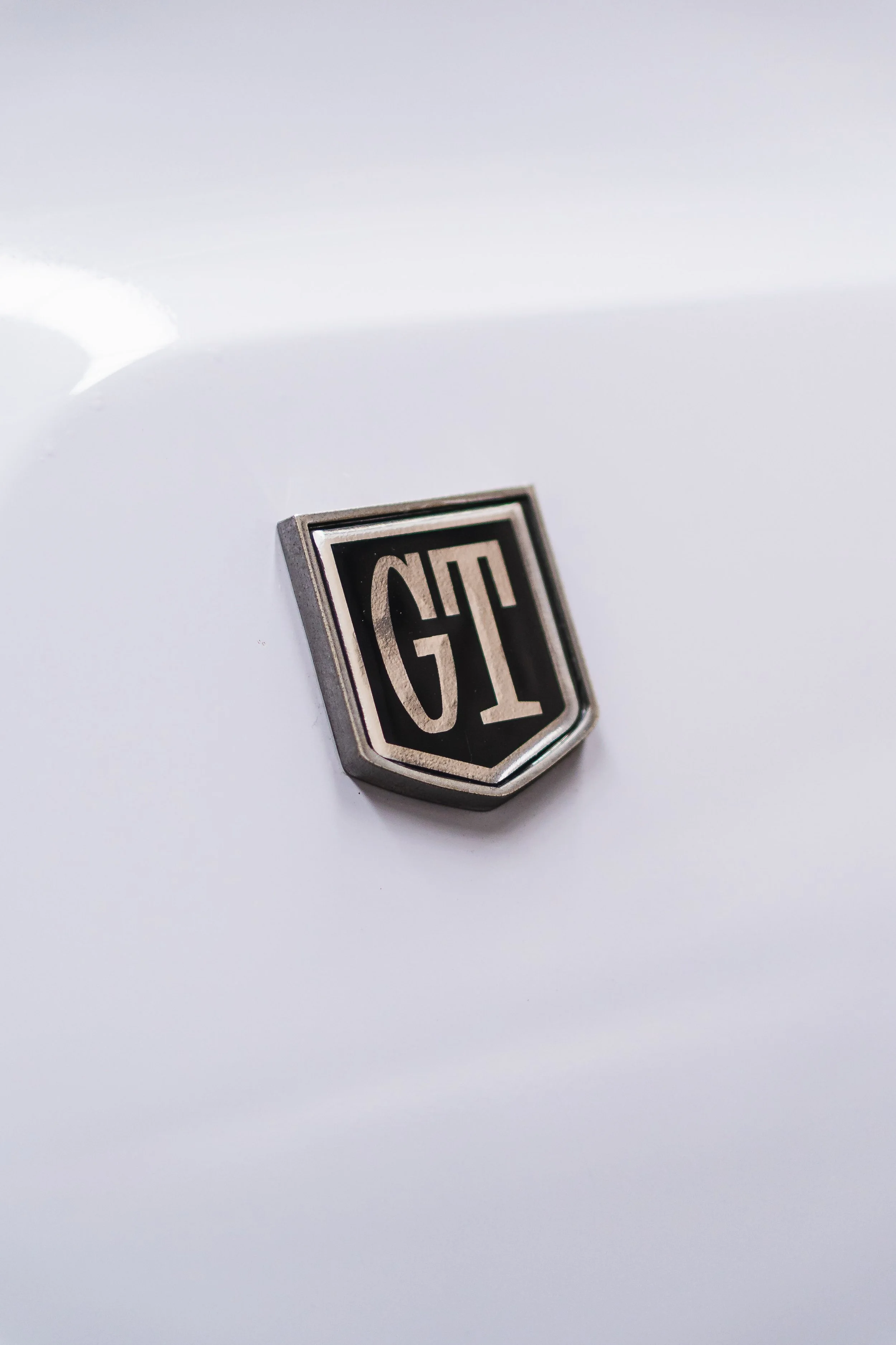 Close-up of a vintage GT badge emblem on a white vehicle.