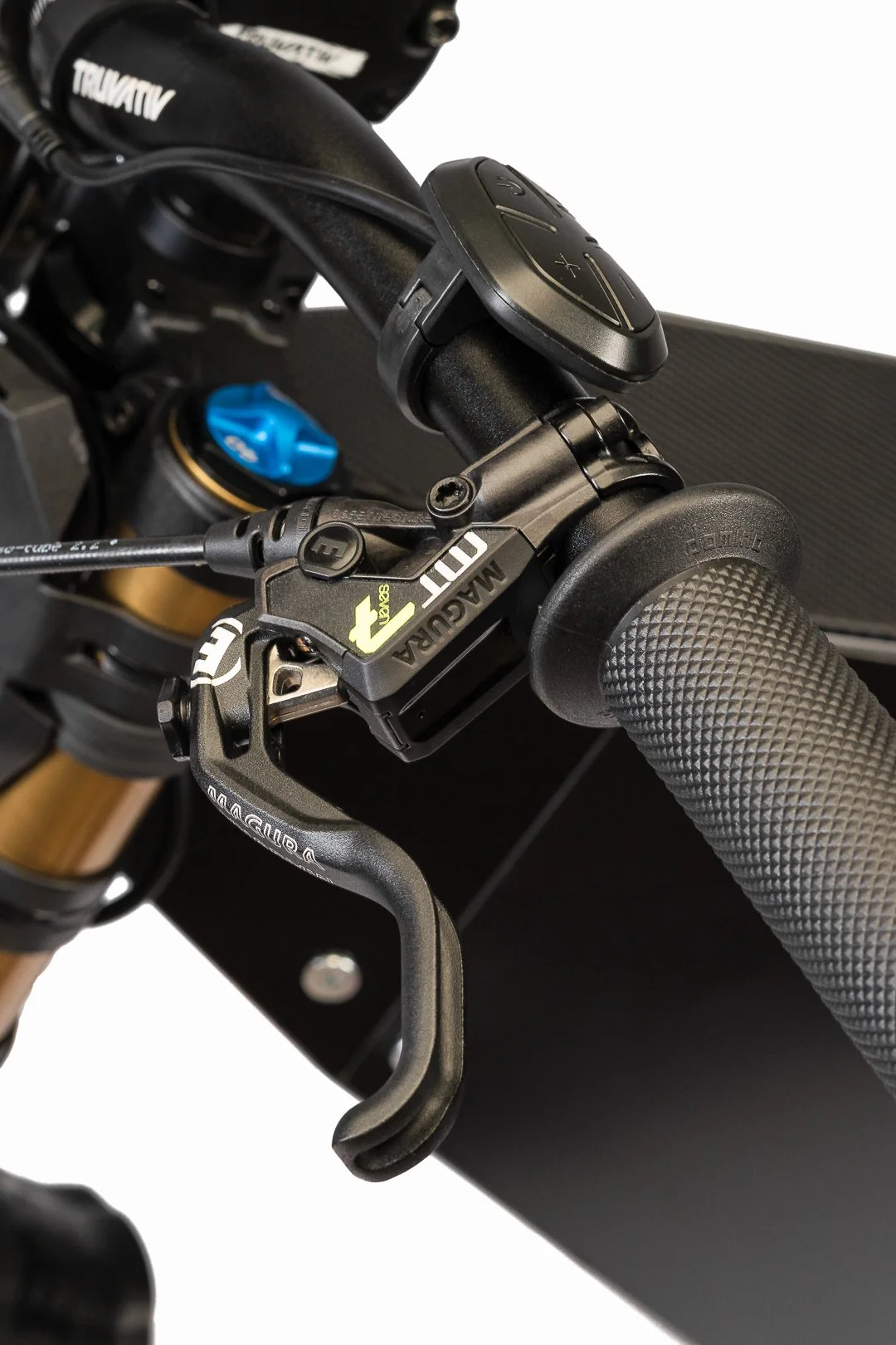 Close-up view of a mountain bike handlebars showing a black handlebar grip, a gear shifter, a brake lever, and a small electronic control device mounted on the handlebar.