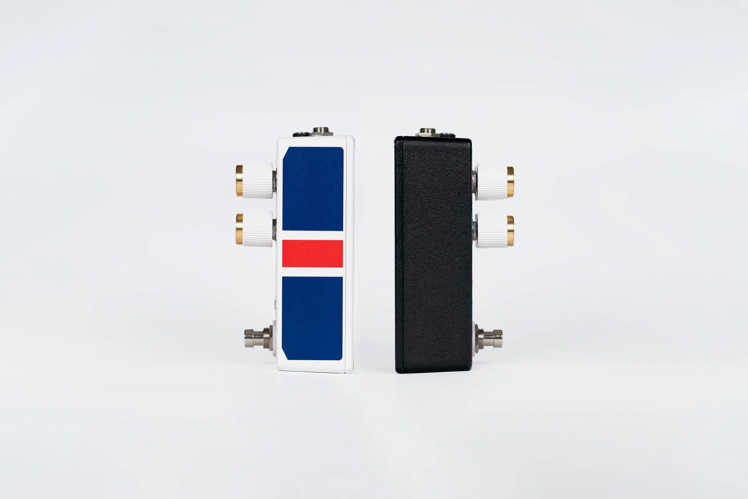 Two guitar effect pedals standing upright on a white background, one black and one white with red and blue sections, with various control knobs on top.