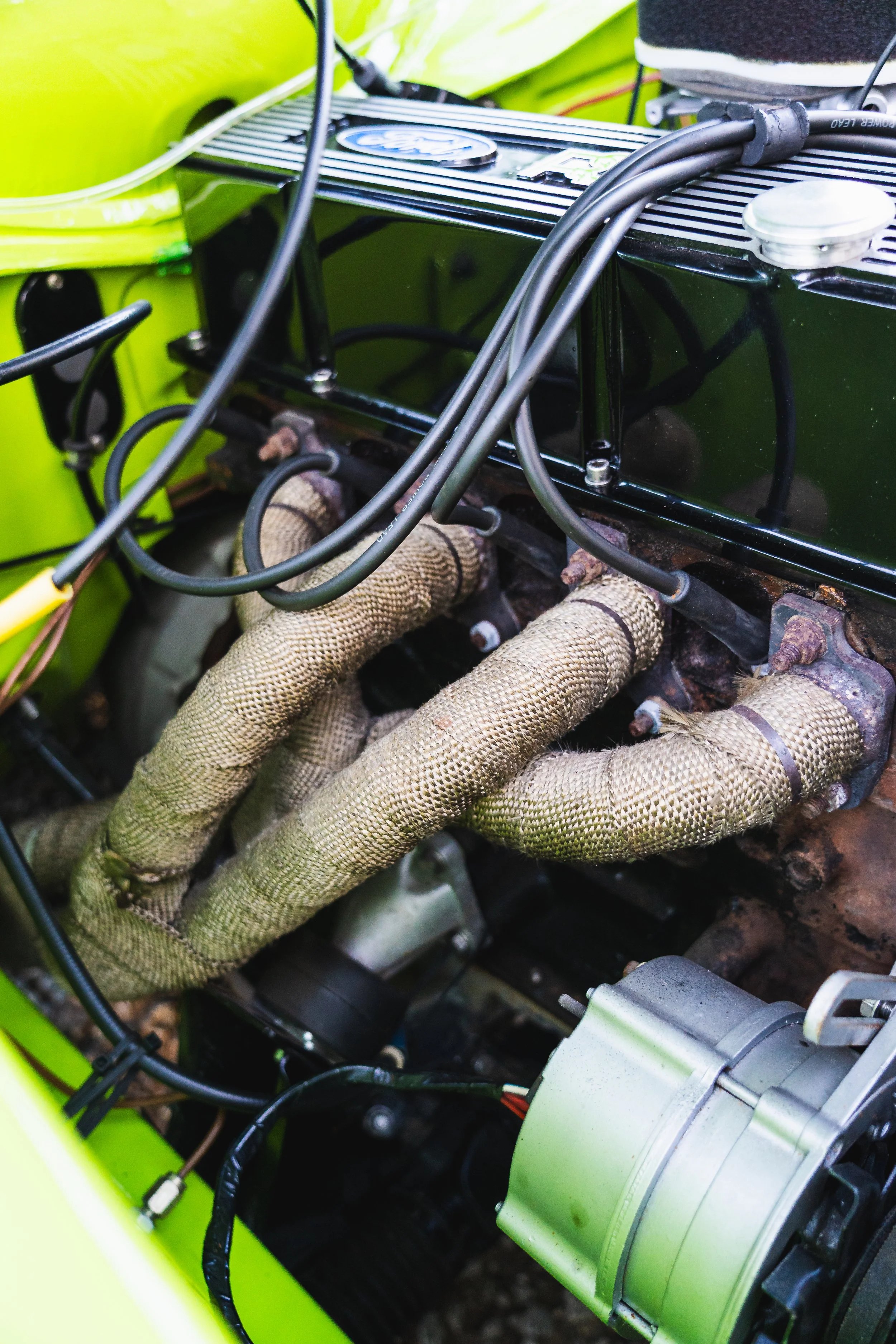 Close-up of a car engine with heat-wrapped exhaust pipes and various other mechanical components.