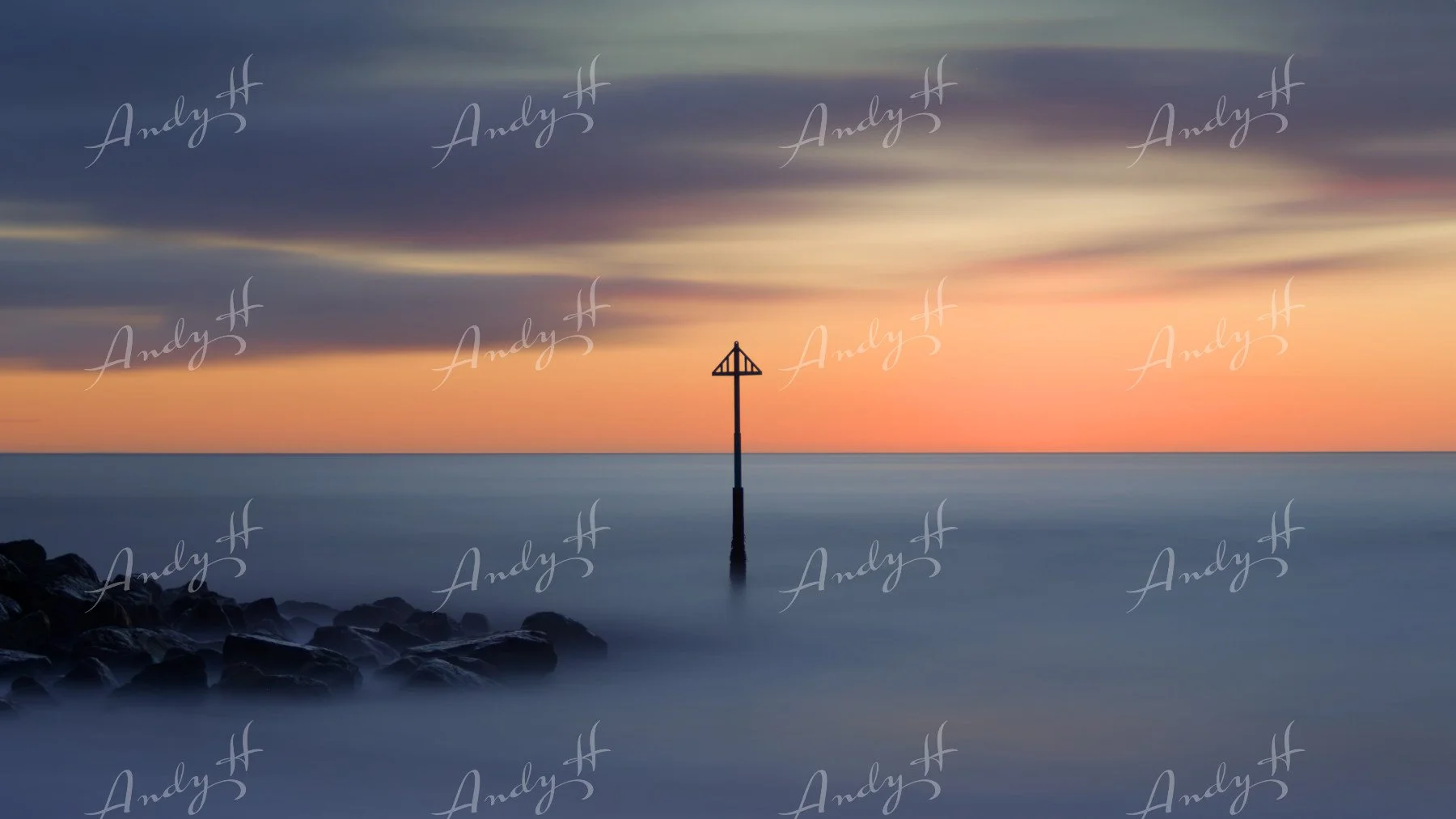 A seascape fine art print, A serene seascape at sunset with a cloud-filled sky, calm ocean water, and a solitary navigation marker or buoy in the water near a rocky shoreline.