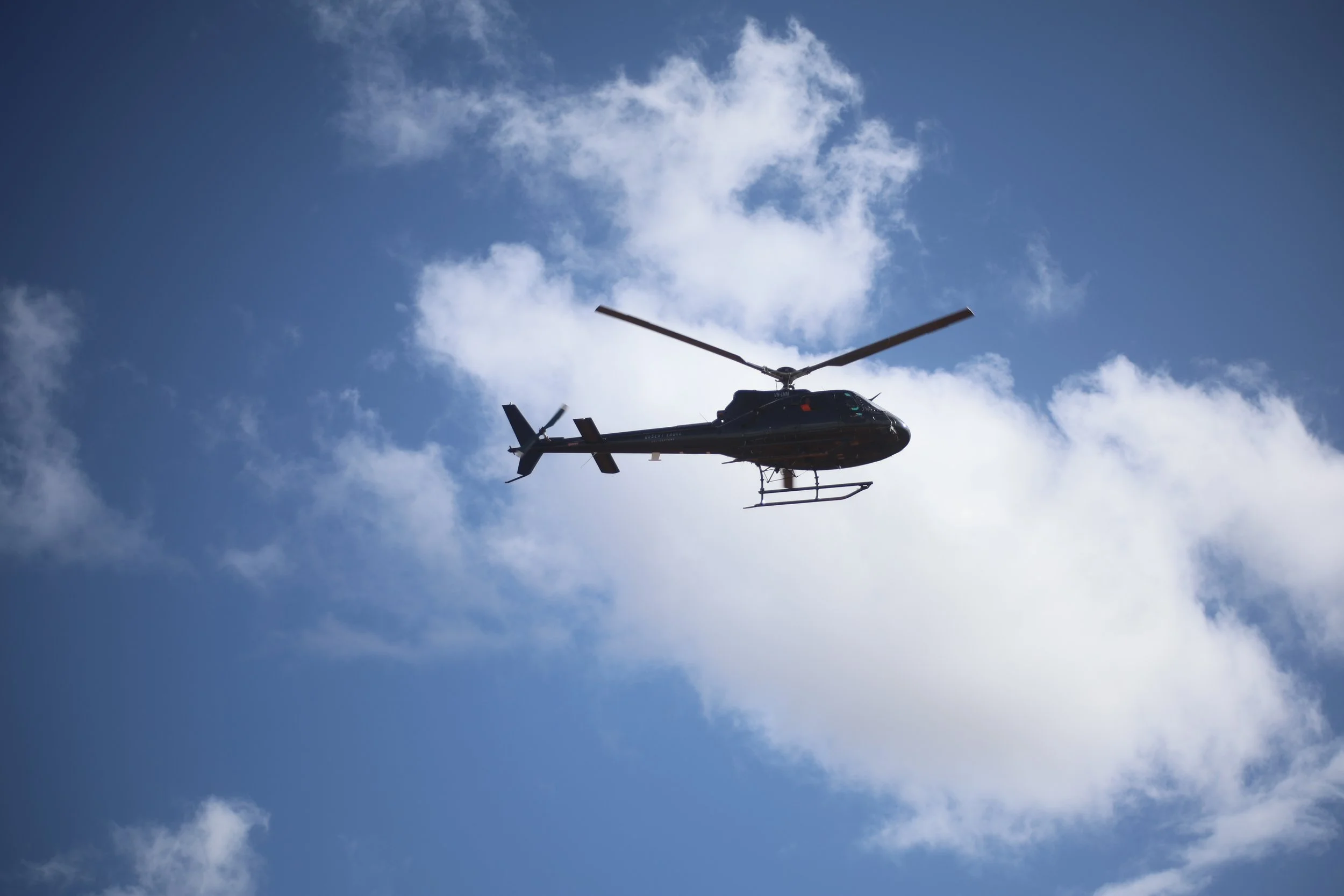 A black helicopter flying in the sky with scattered clouds.