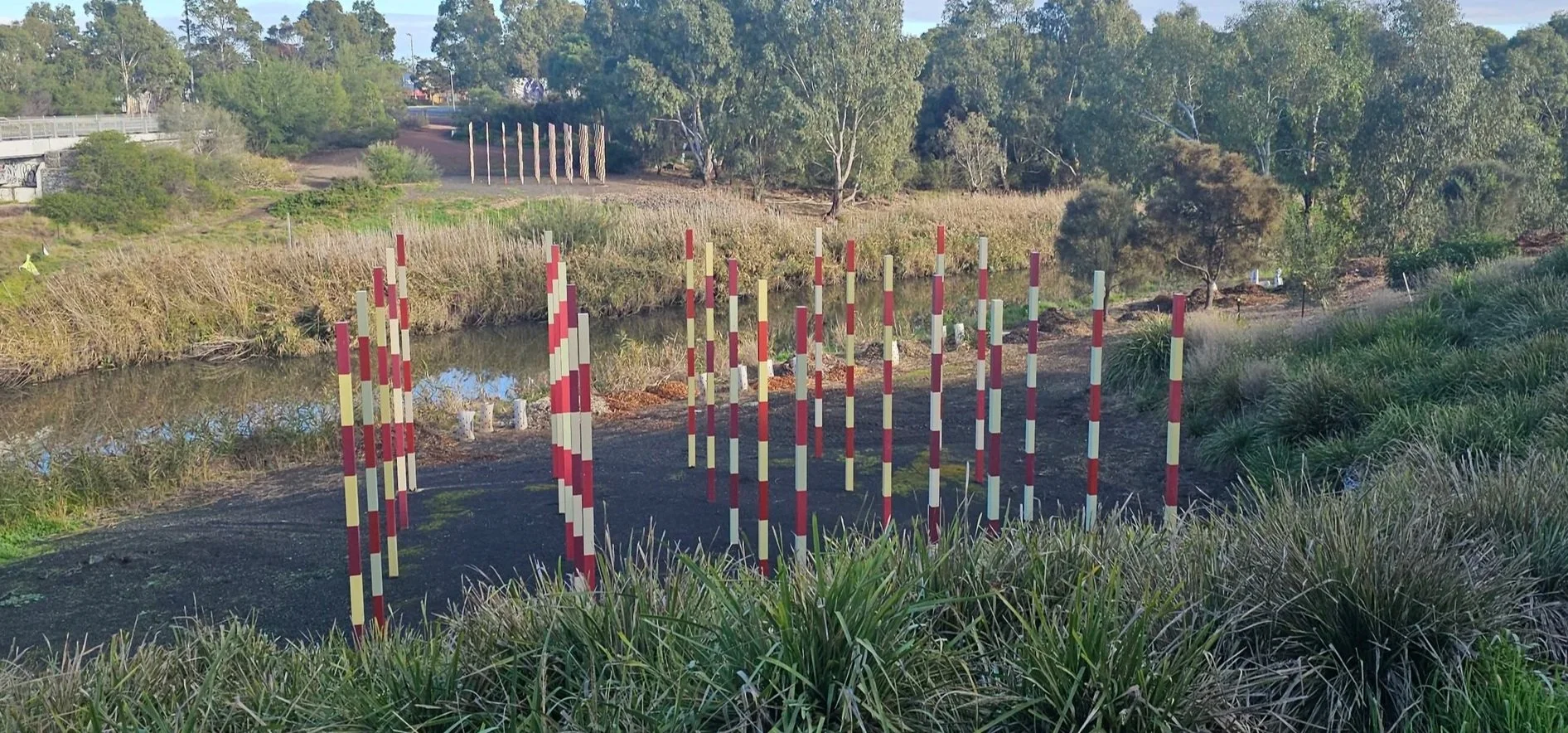 A pathway with guard posts leading over a small body of water, surrounded by trees and bushes.