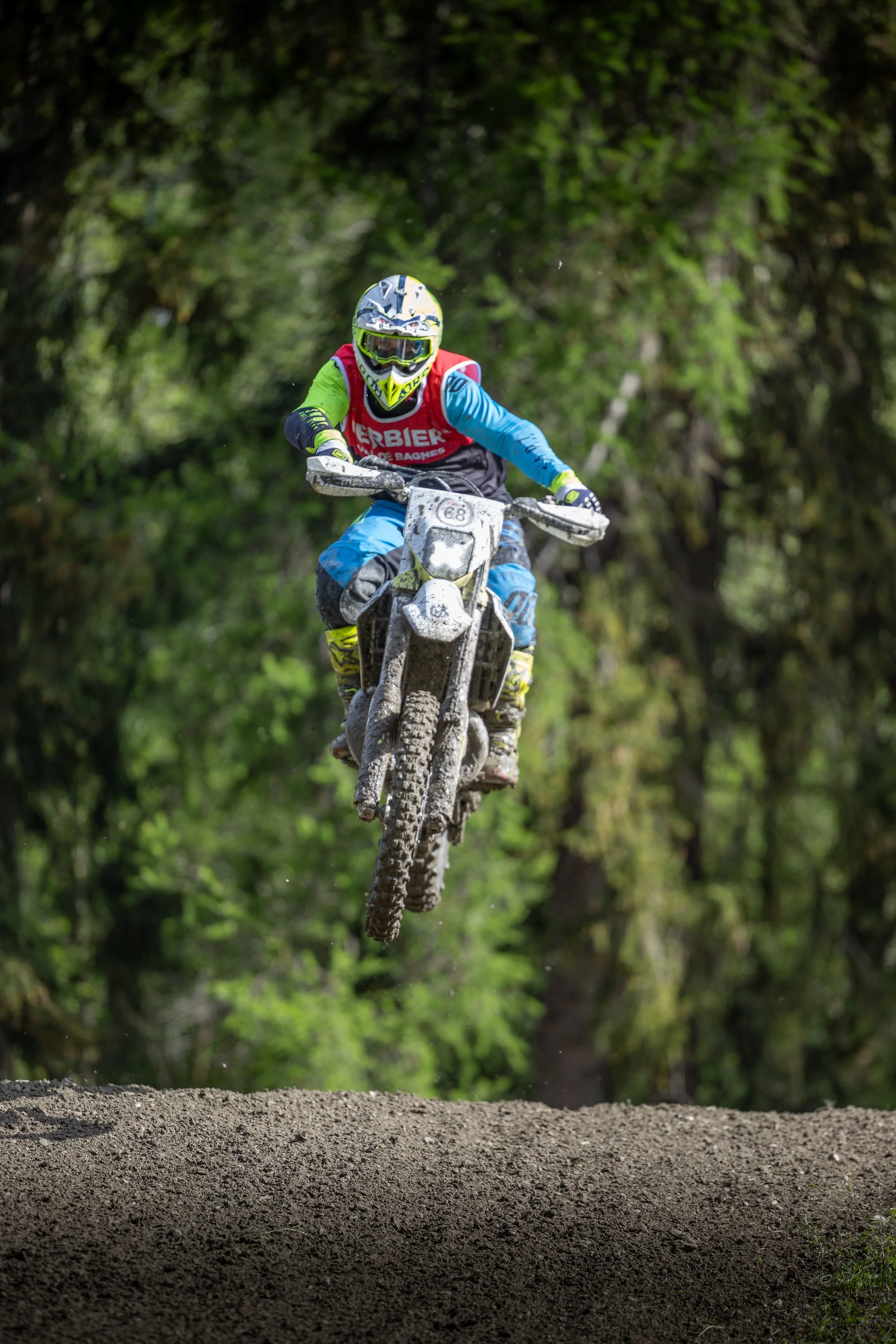 Off-road motorcycle rider in helmet and riding gear jumping over dirt trail in wooded area.