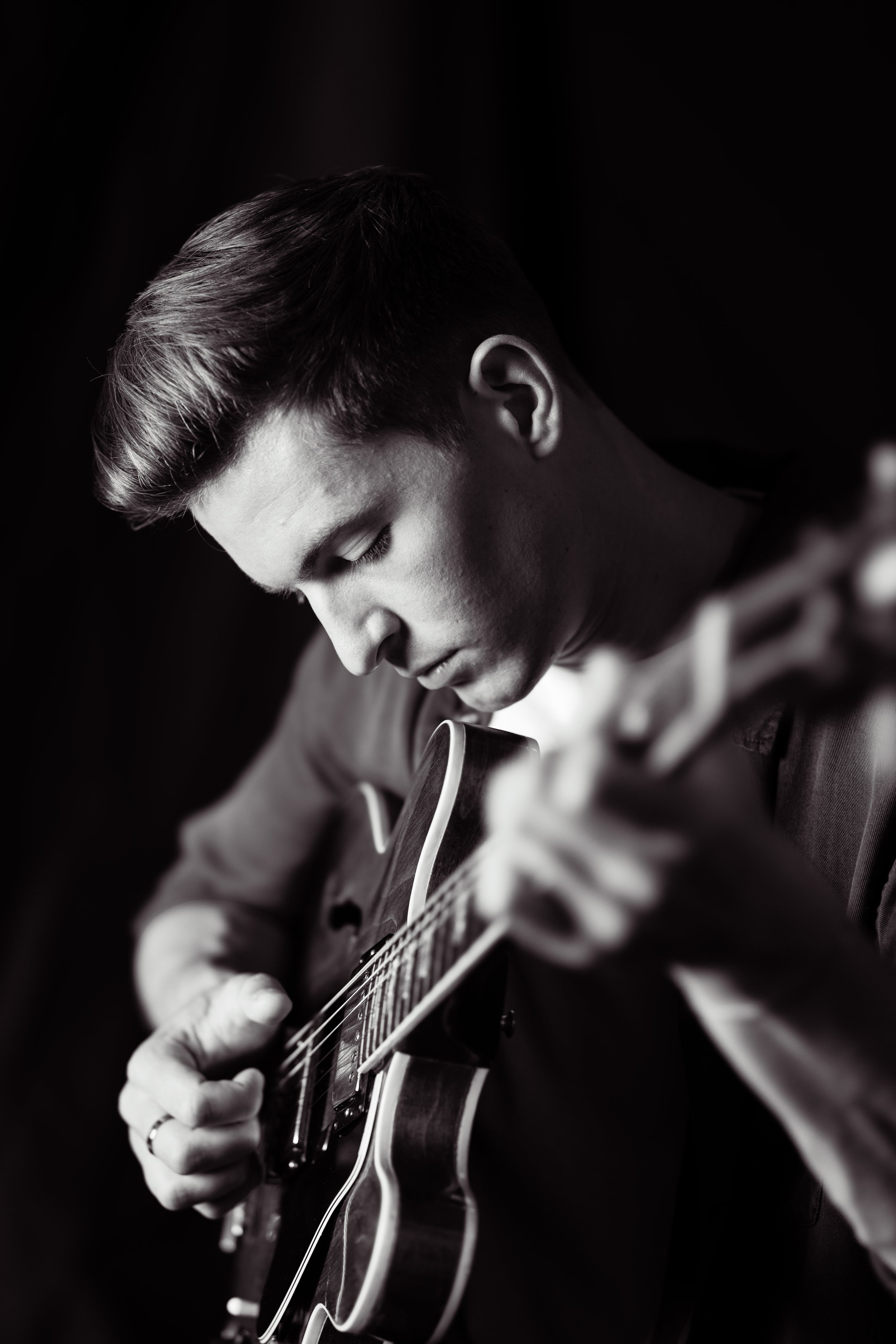 Black and white photo of a young man with short hair playing an electric guitar, focused on his strumming.