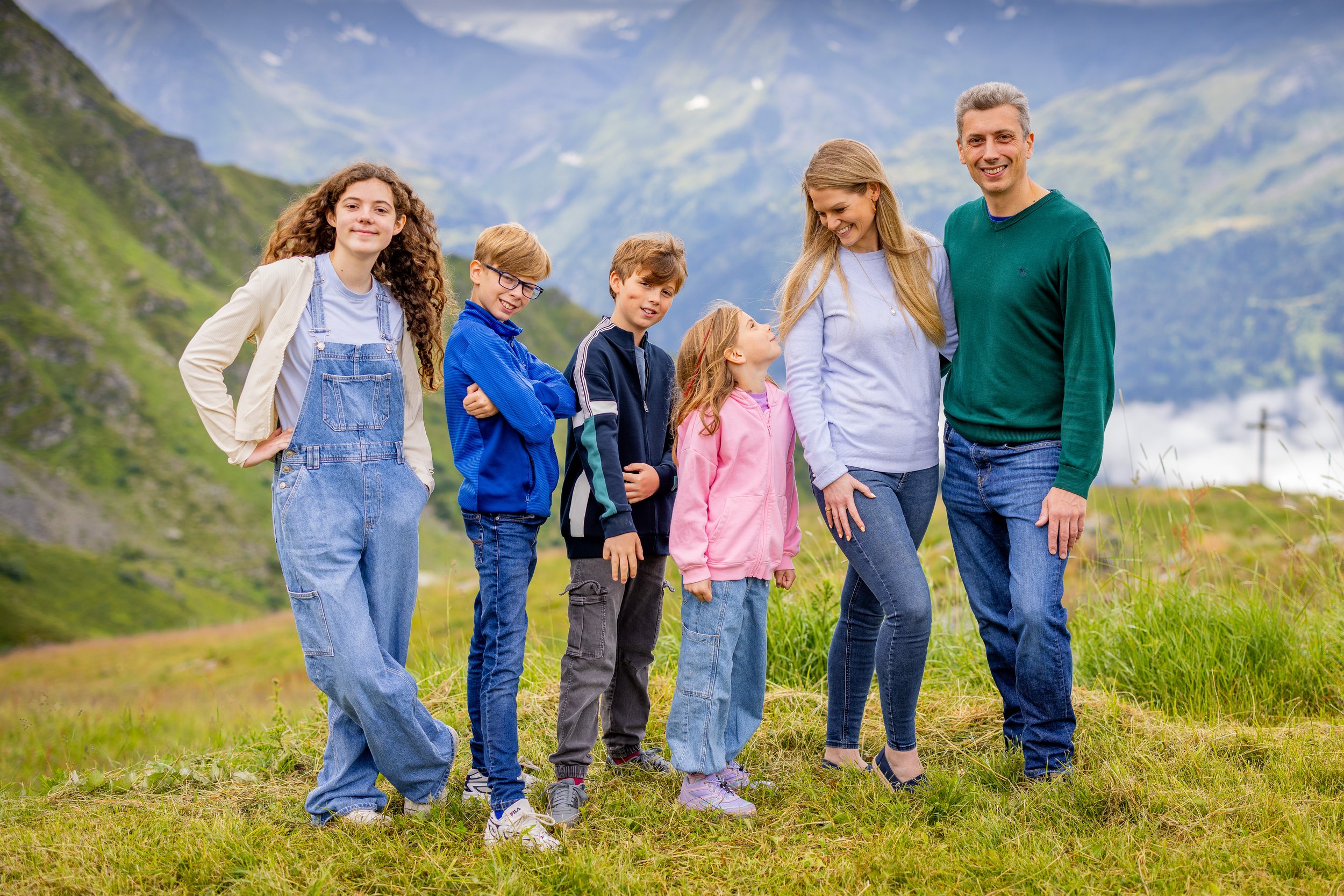 Family of seven outdoors in a green mountainous landscape, smiling and interacting with each other based in Verbier Switzerland