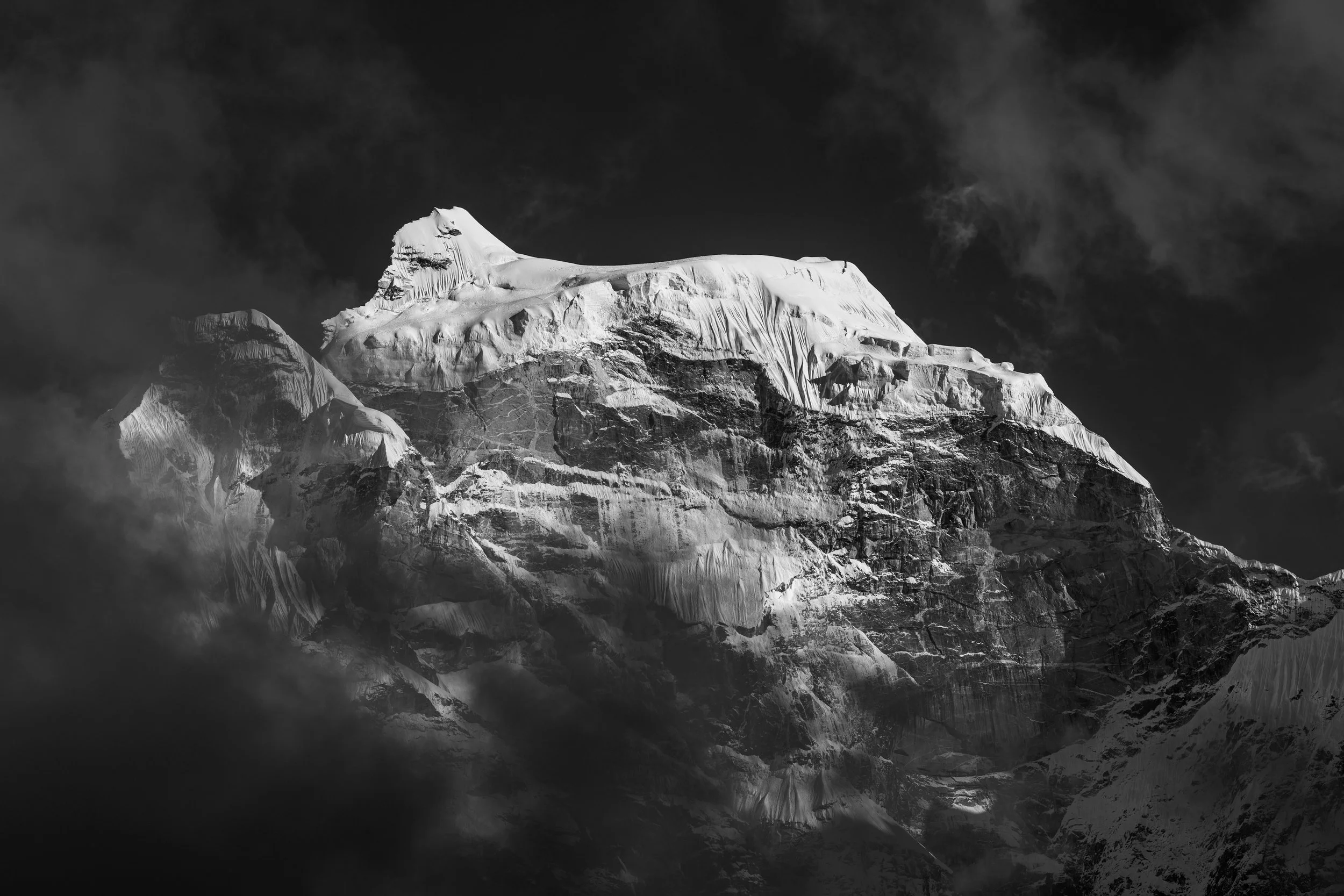 Black and white photo of a snow-capped mountain peak surrounded by dark clouds.