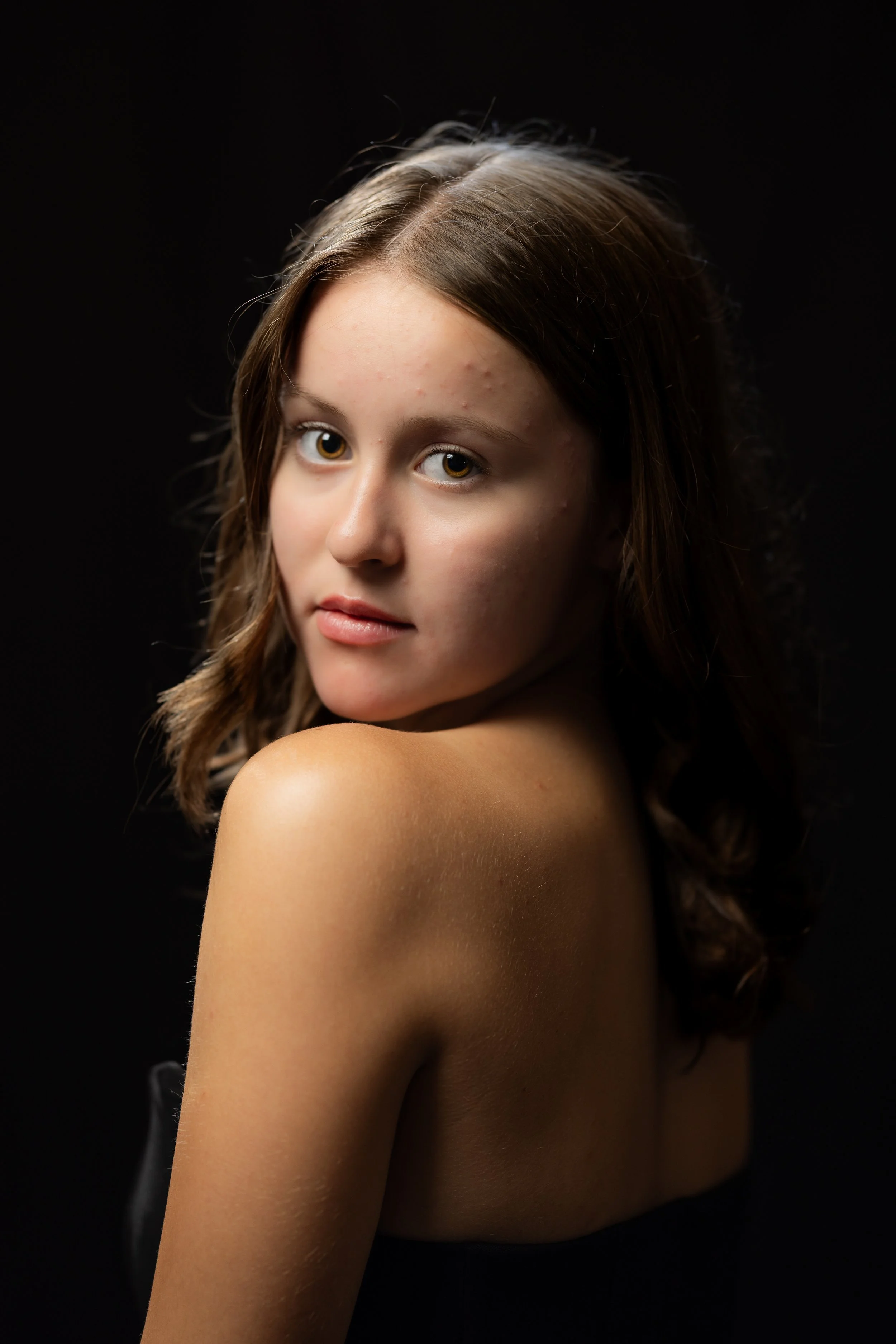 A young woman with light brown hair and fair skin looking at the camera against a dark background.