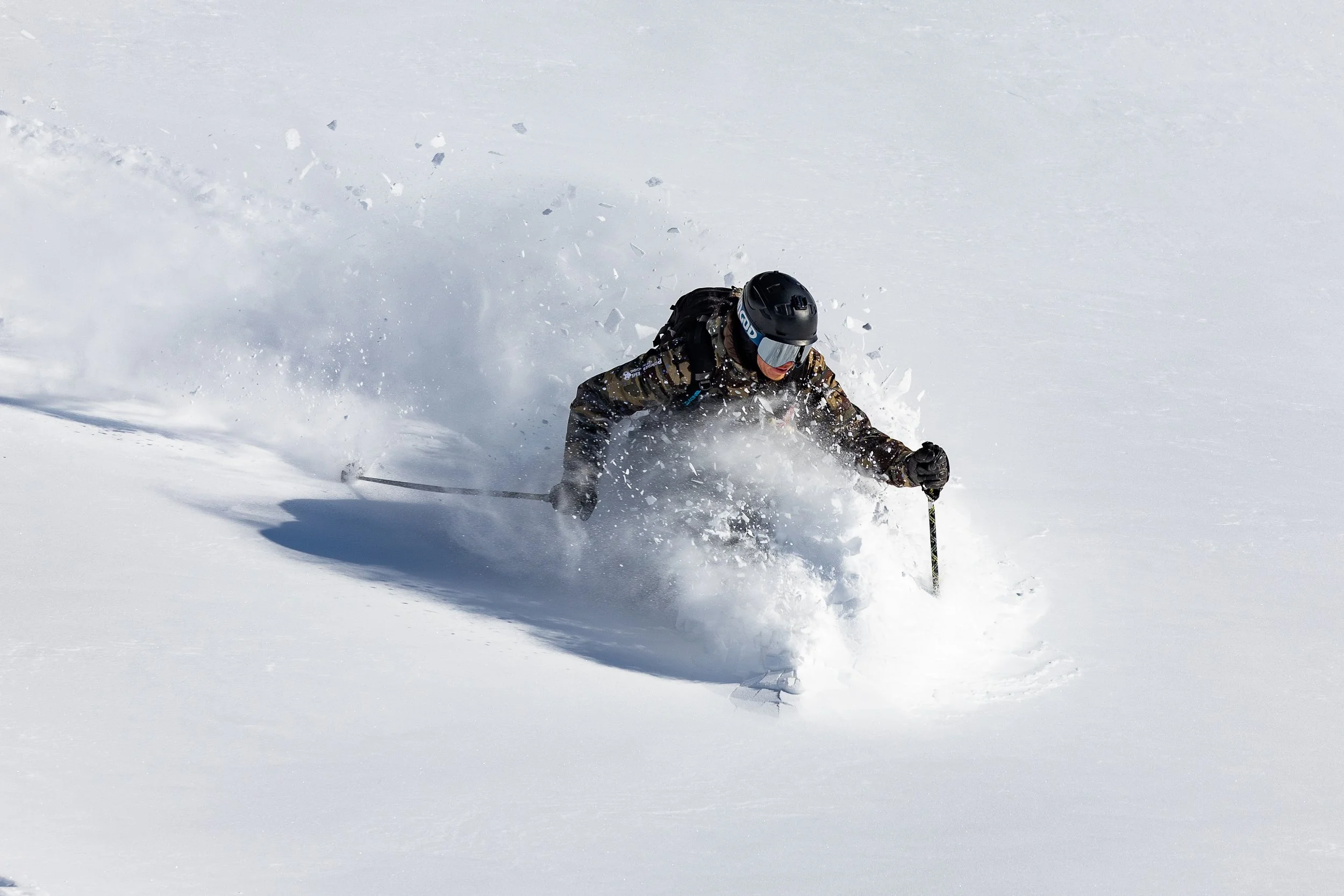 A skier in black gear and helmet skiing down fresh powder snow.