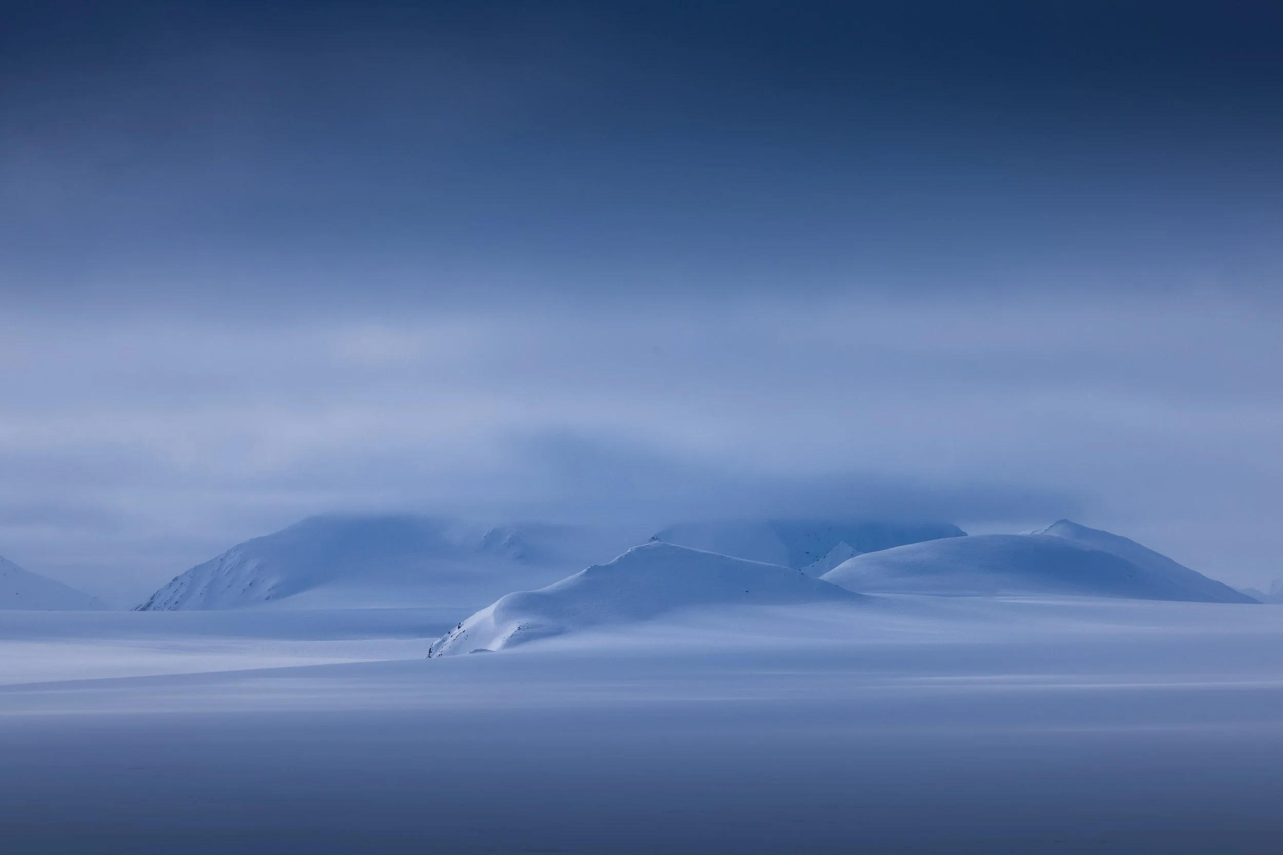 Snow-covered mountains under a cloudy sky in a cold, arctic landscape.