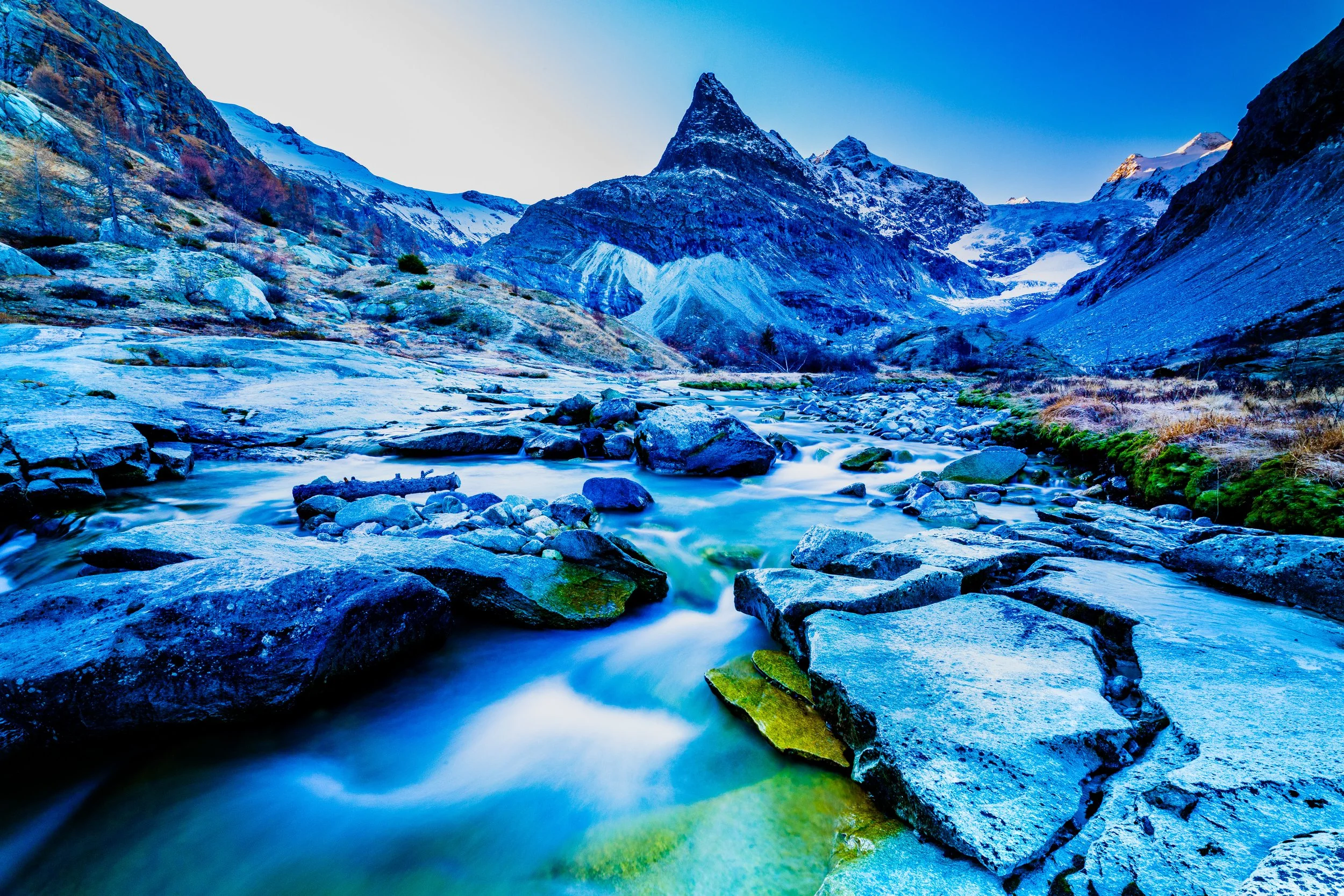 Snow-capped mountains and a flowing river in a rugged, rocky valley.