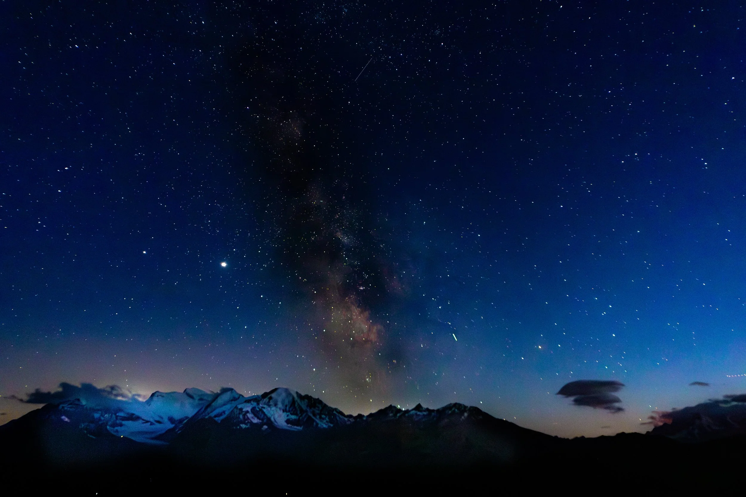 Night sky filled with stars over snow-capped mountains and clouds.