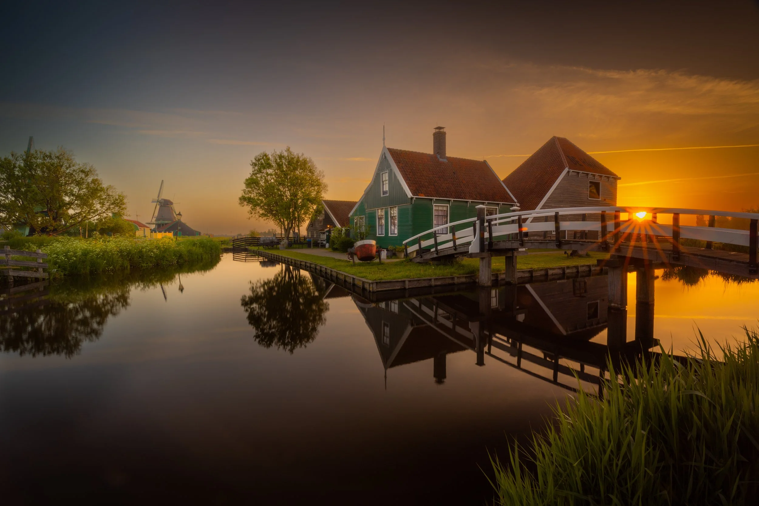 Sunset over traditional Dutch houses and windmill next to a canal in a rural village