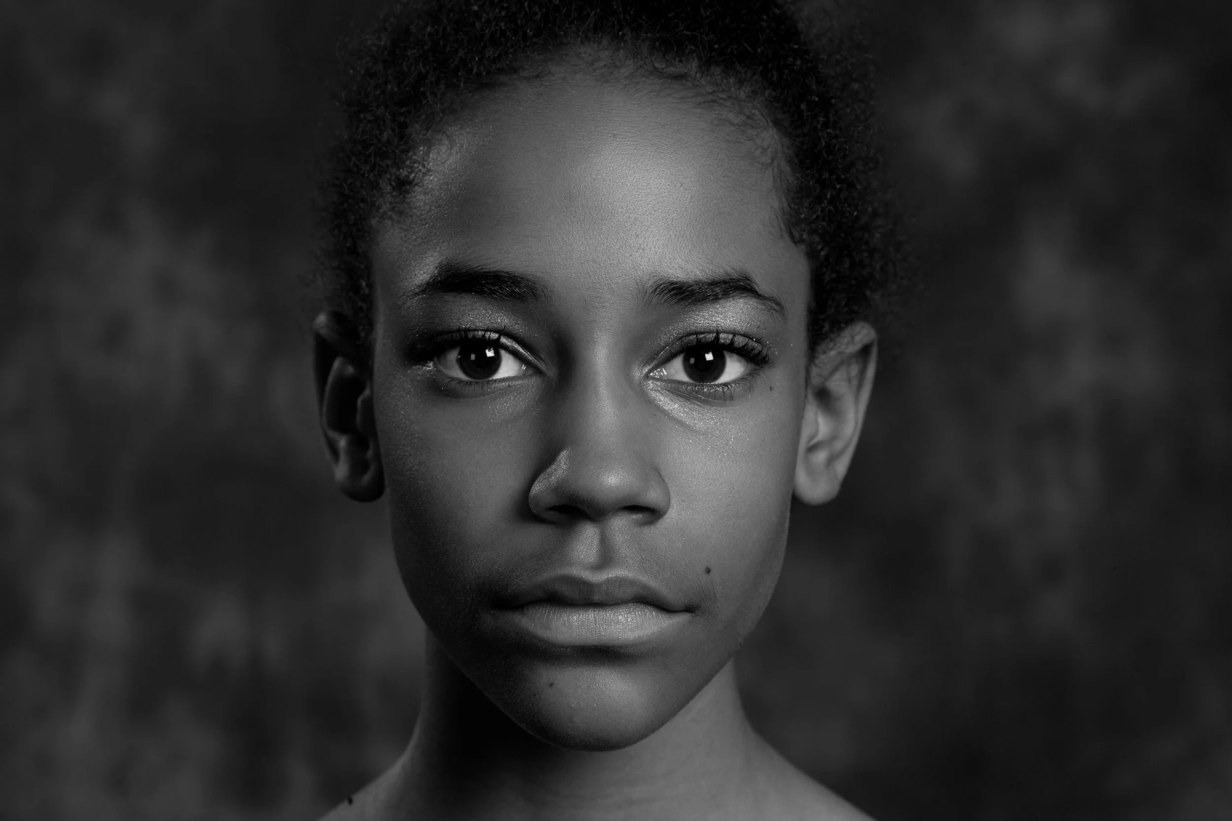 Black and white close-up portrait of a young girl with short curly hair, looking directly at the camera.