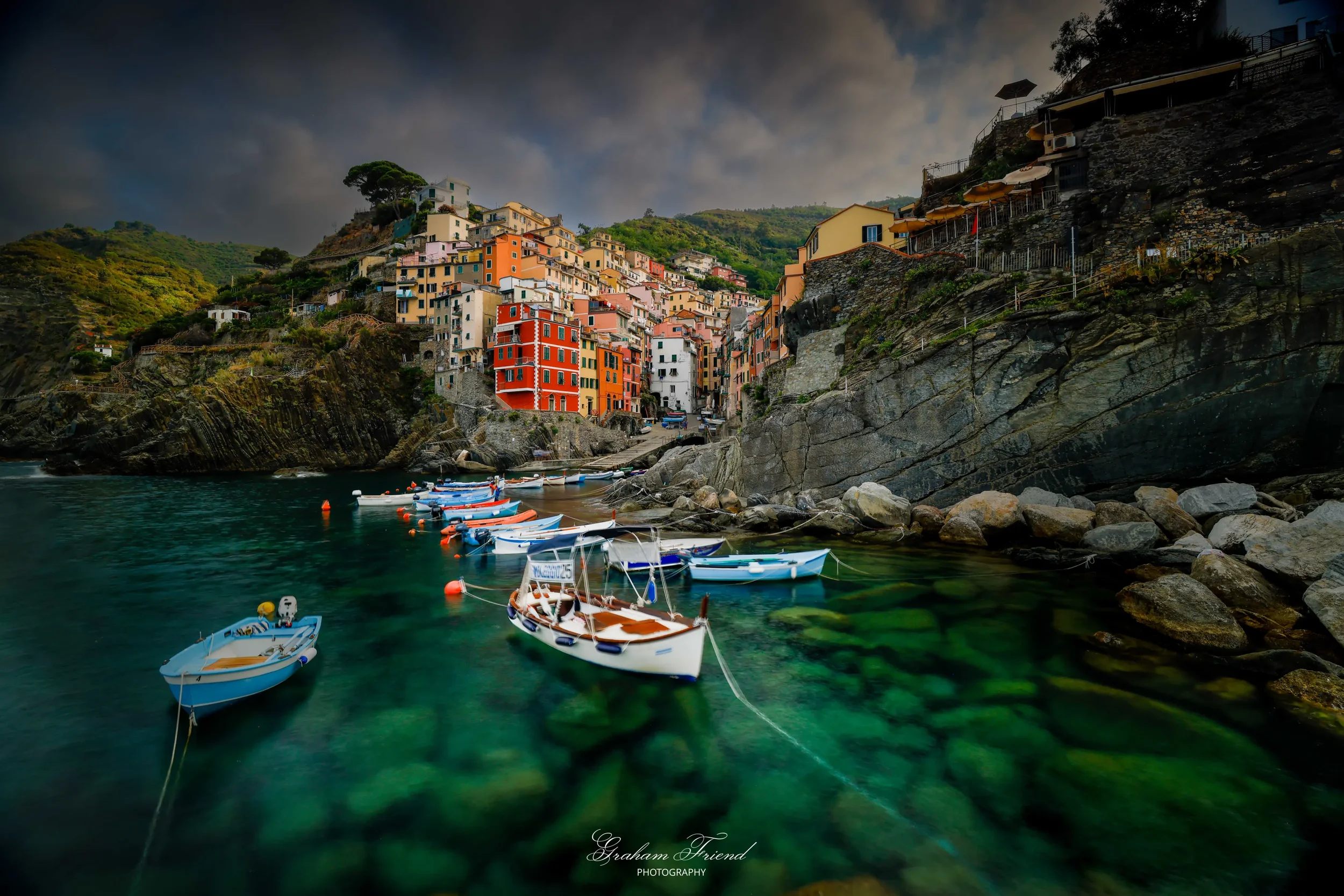 Colorful houses on a hillside overlooking a small harbor with boats in clear green water in Cinque Terre, Italy.