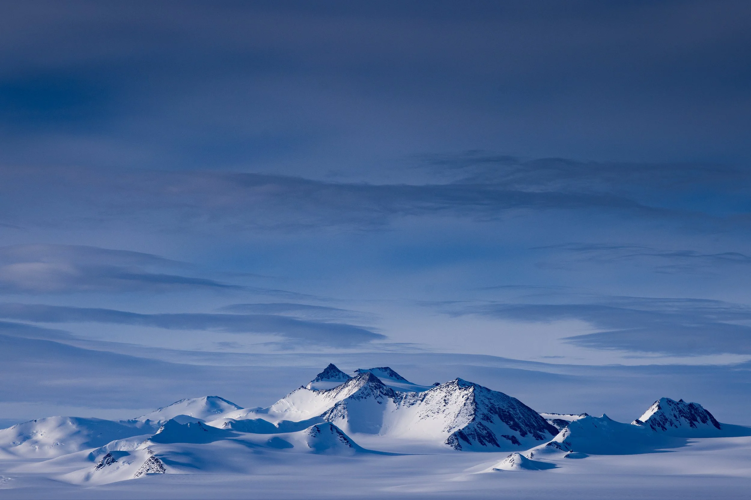 Snow-covered mountain range under a blue sky with scattered clouds.