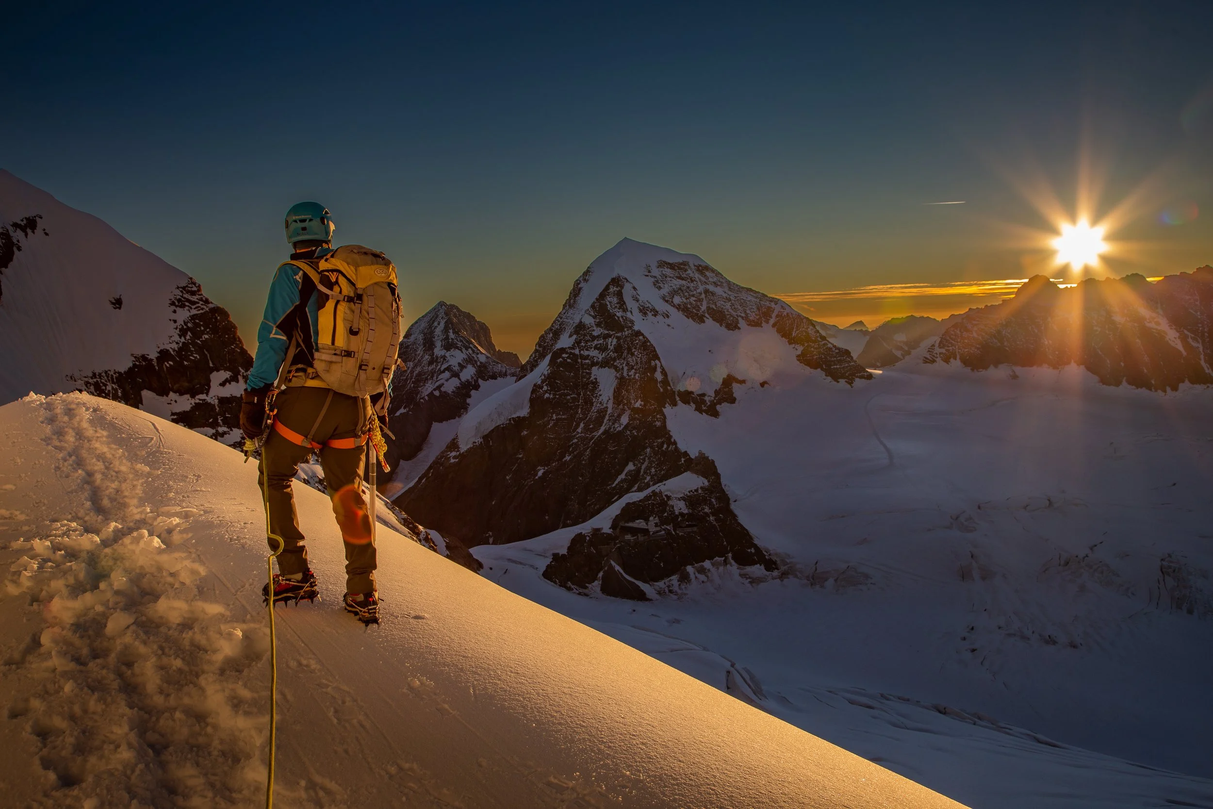 Mountaineer climbing snowy mountain ridge during sunset in the mountains.