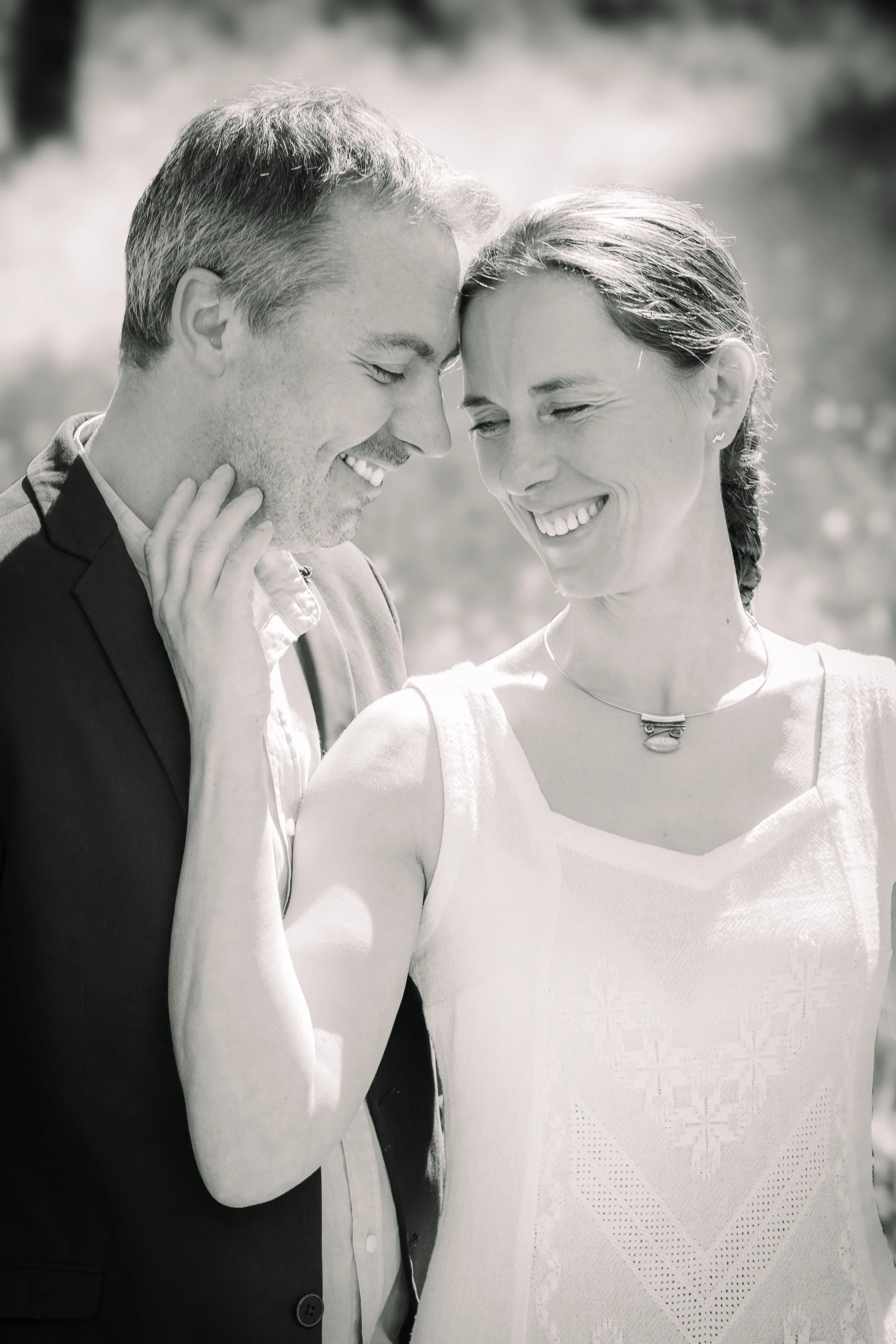 A black-and-white photo of a man and woman close together, smiling and touching foreheads in a tender moment outdoors.