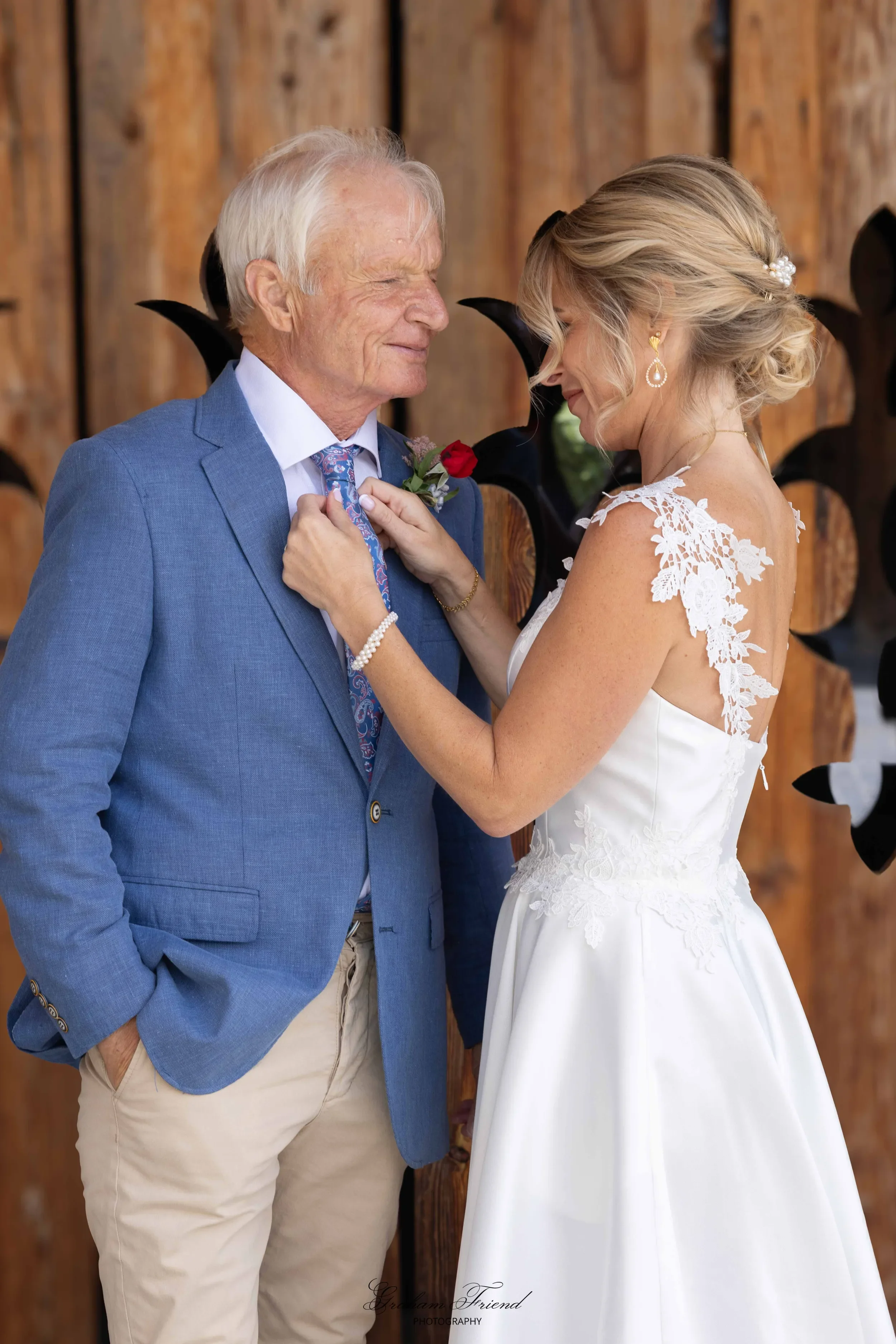 A woman in a wedding gown adjusting an older man's tie during a wedding ceremony.