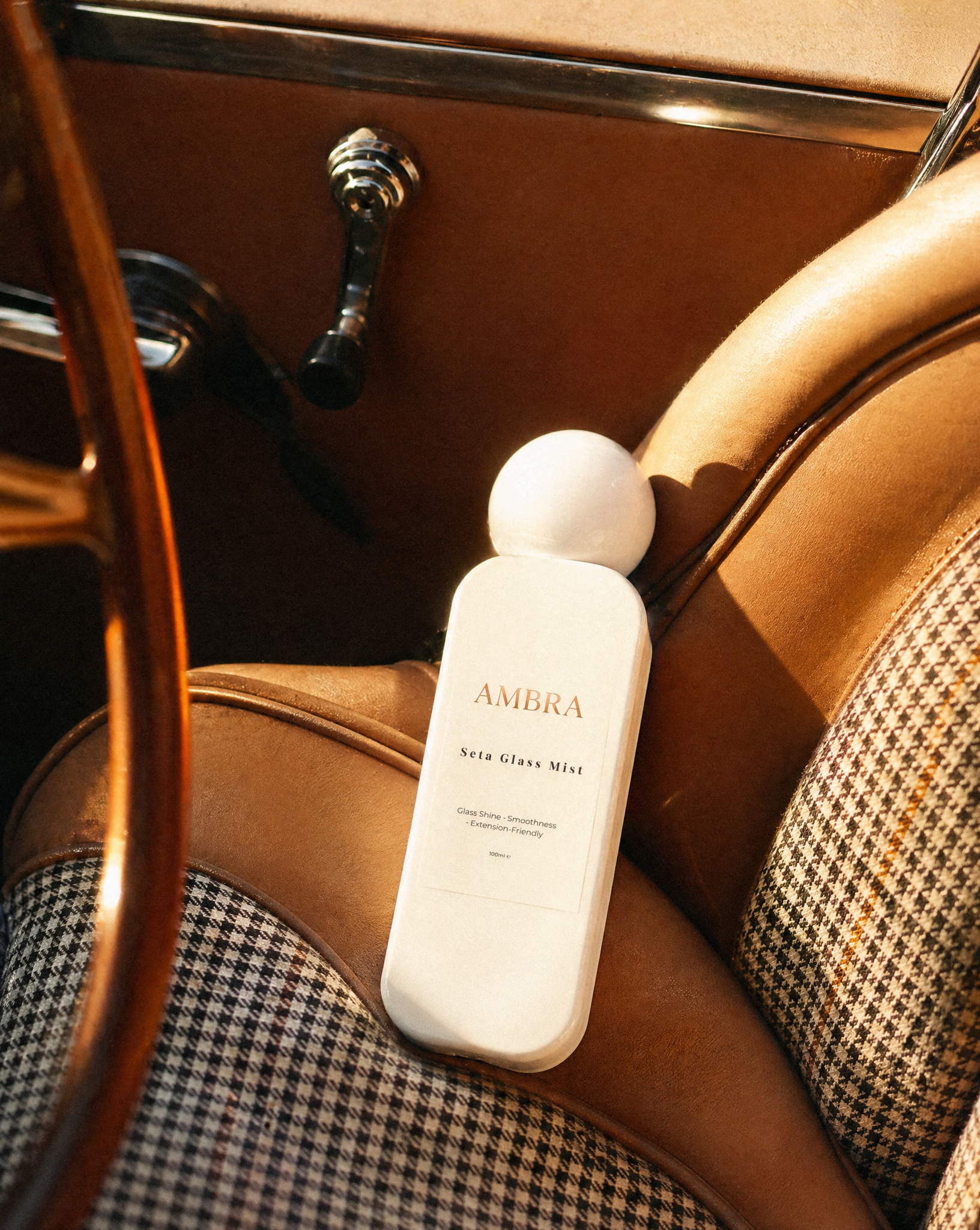 Close-up of a vintage car interior with a gear shift, brown leather upholstery, and a white bottle labeled 'AMBR'A Seta Glass Mist.