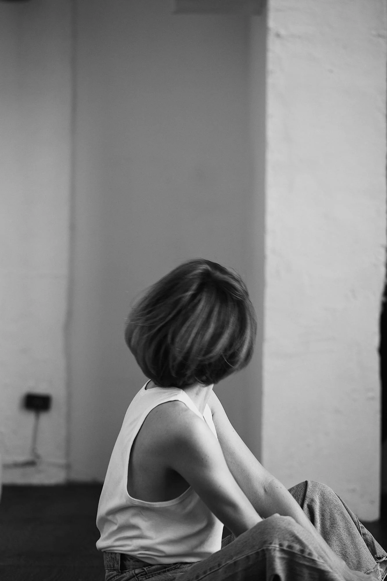black and white image woman sitting on ground looking away in white tank and jeans